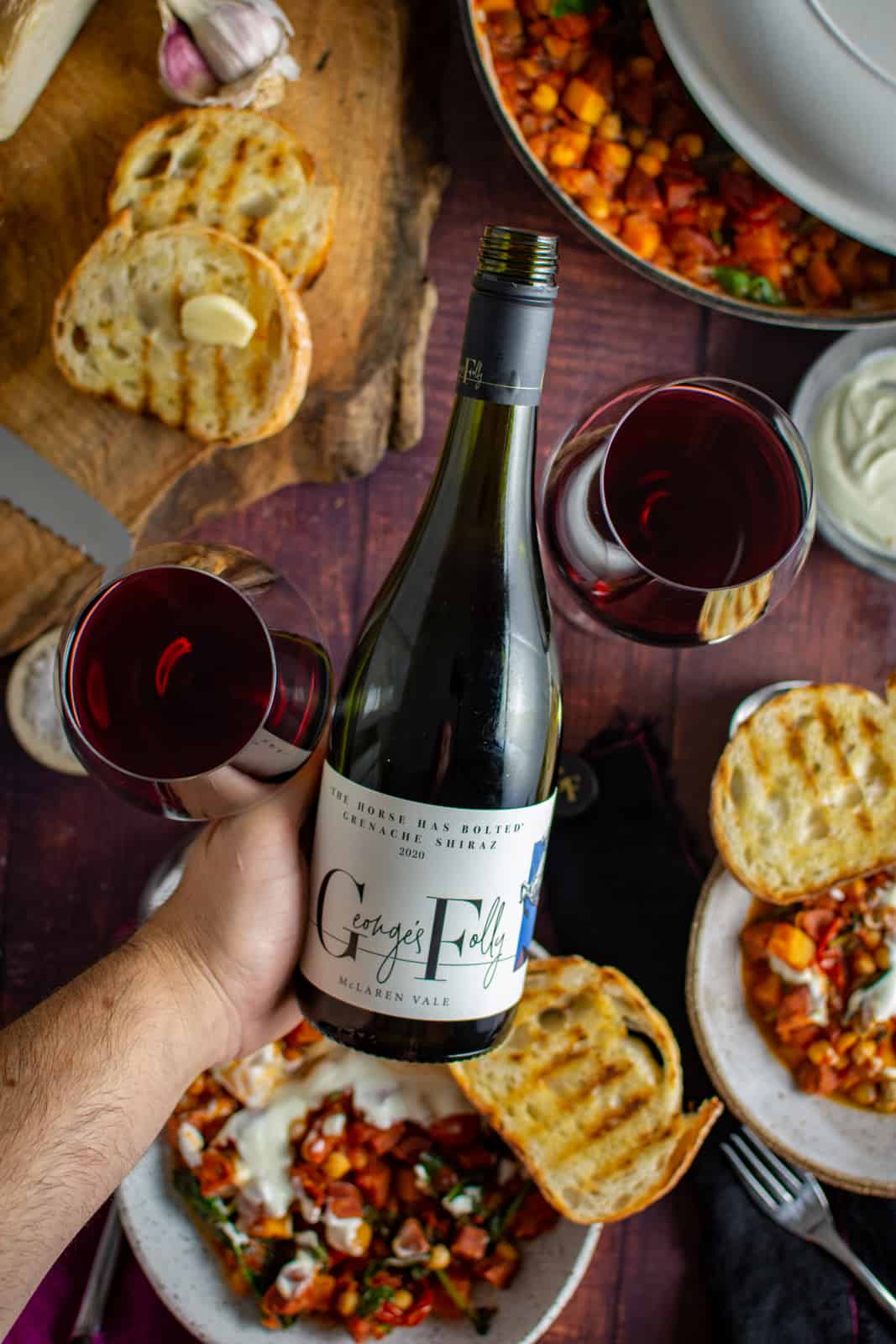 someone holding georges folly wine with food on table in background