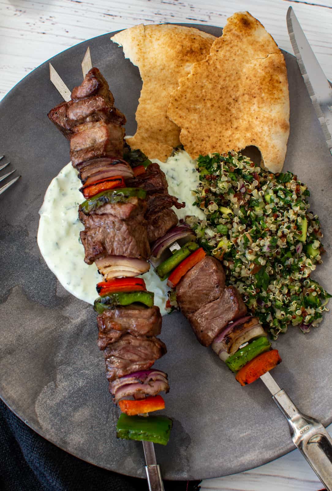 grilled lamb kebabs, tabbouleh, yoghurt dressing and pita on a plate