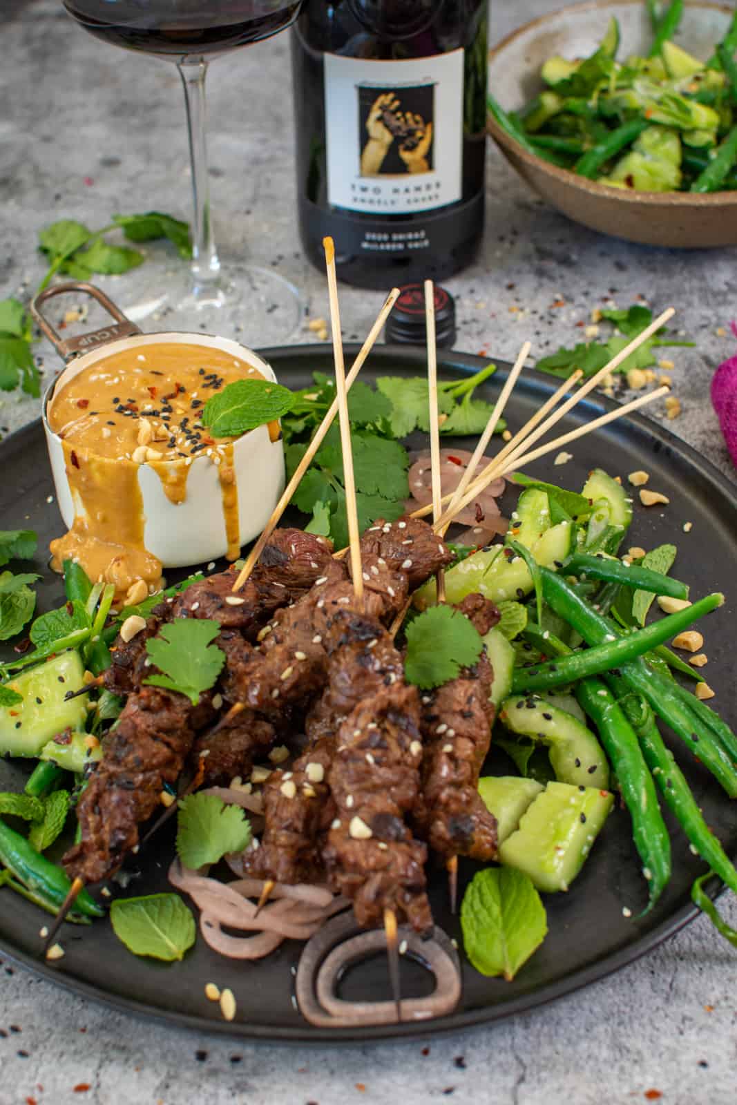 close up of beef satay skewers with satay sauce and cucumber salad