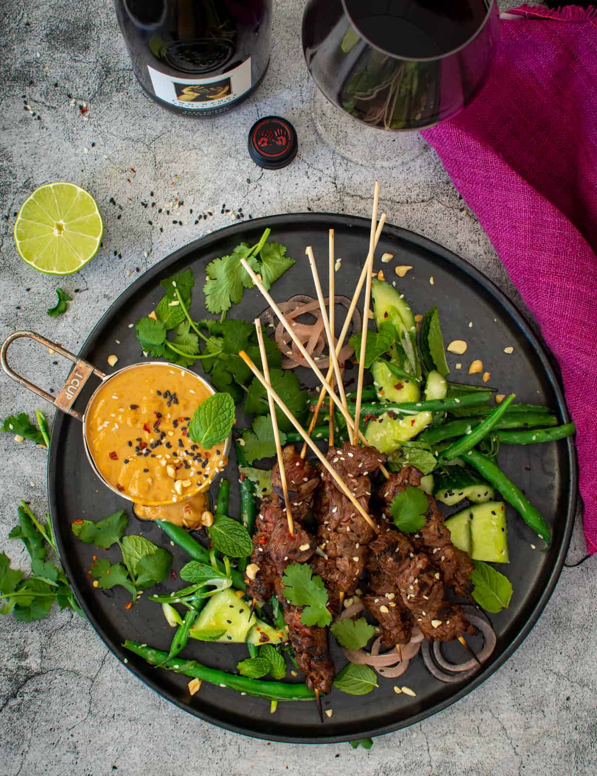 a plate of beef satay skewers wit cucumber salad and satay sauce