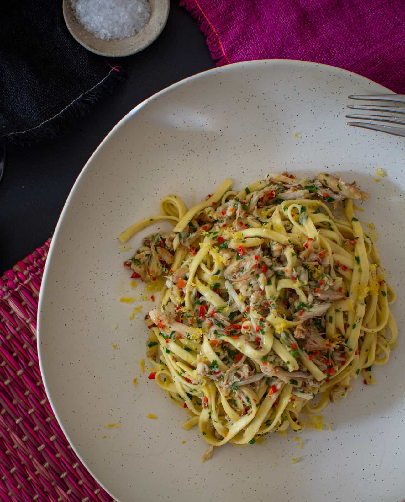 a white bowl filled with chilli crab pasta on table mat 