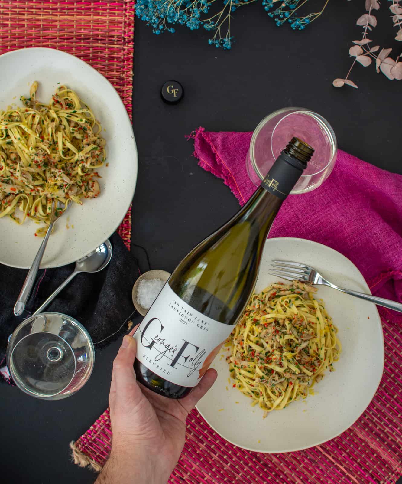 Someone pouring glass of wine with bowls of pasta below