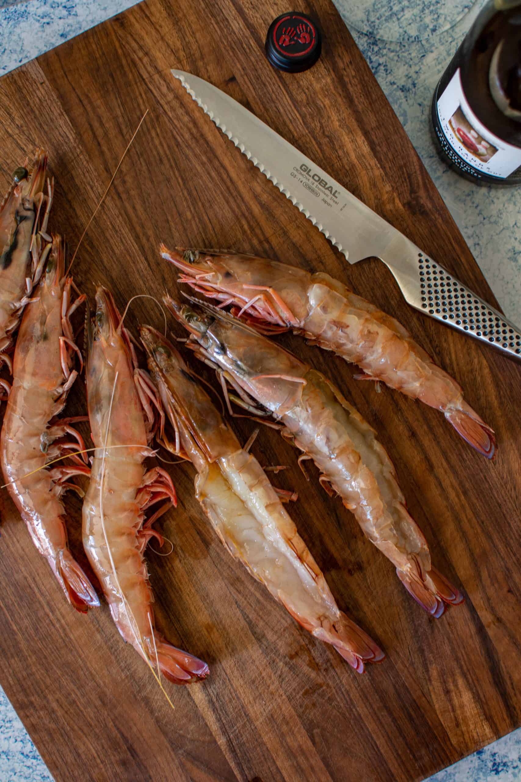 raw prawns on a chopping board with global chef knife and bottle of wine next to board
