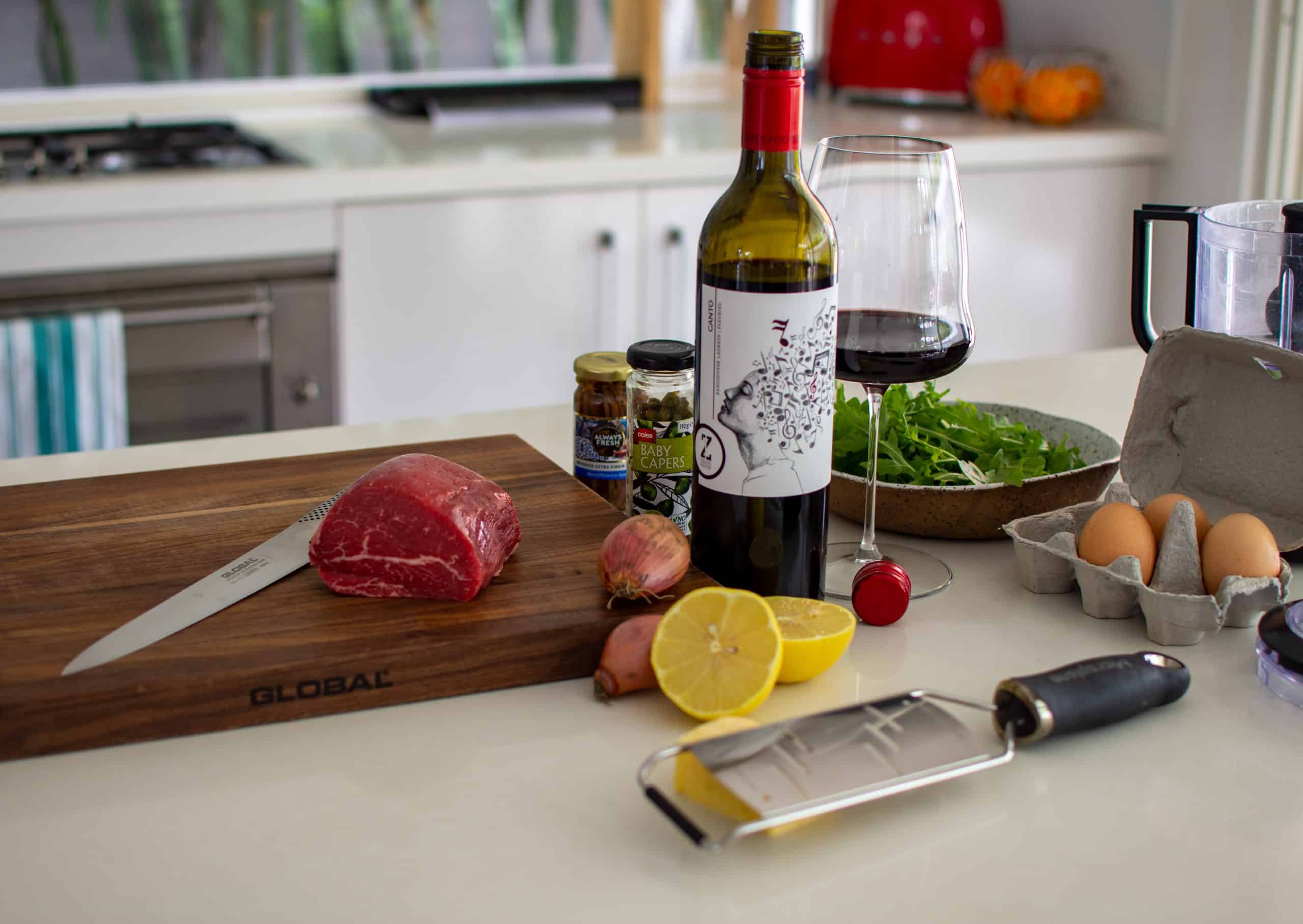 beef tenderloin on a chopping board with carpaccio ingredients and red wine on kitchen counter top