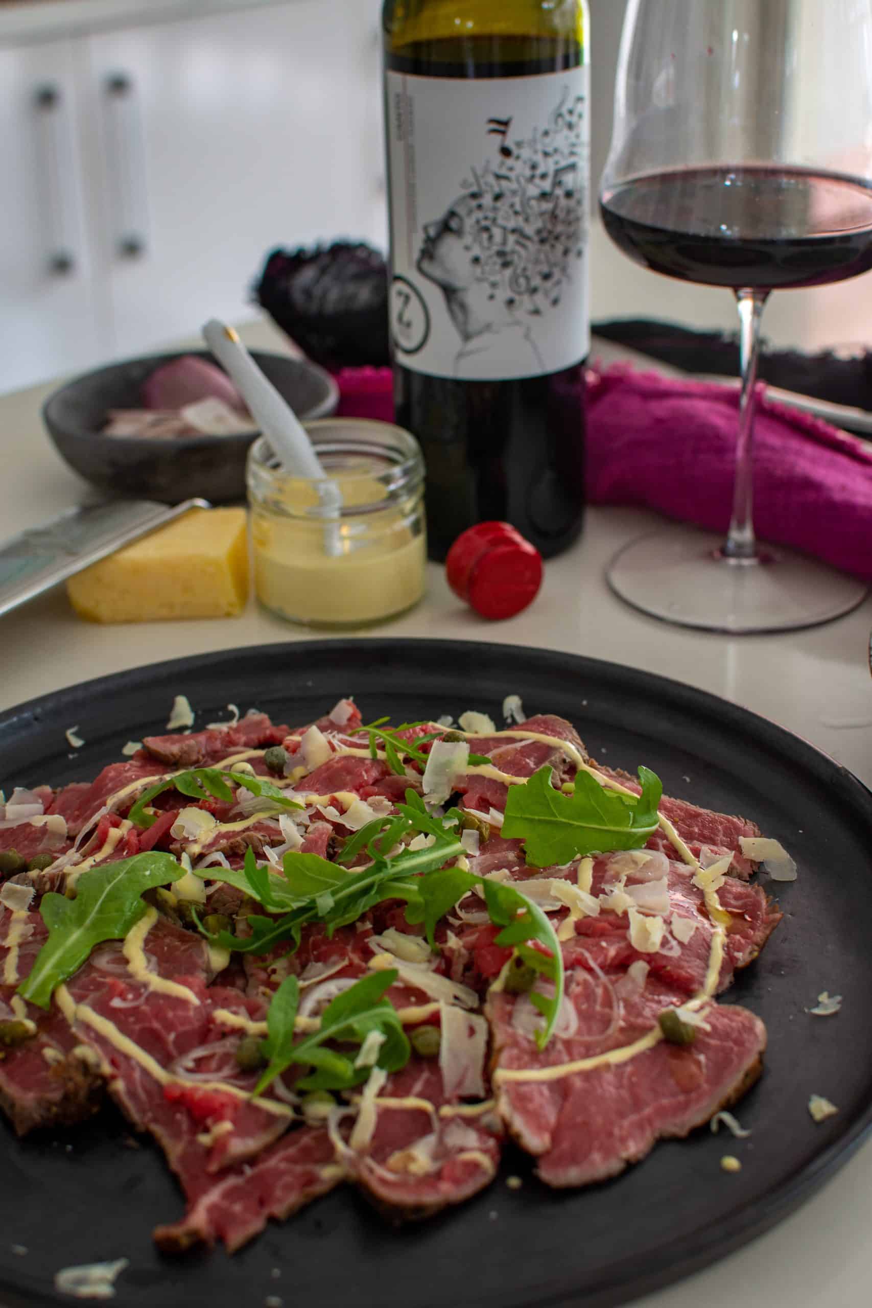 A plate of beef carpaccio with red wine in background