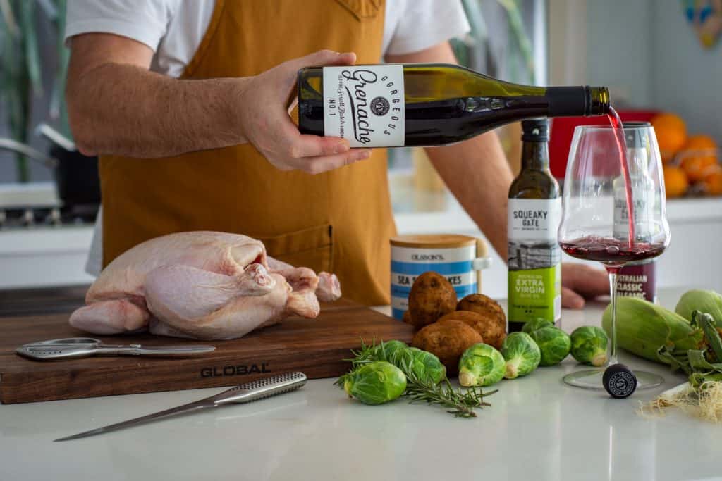 pouring a glass of wine in the kitchen with chicken and vegetables on the counter