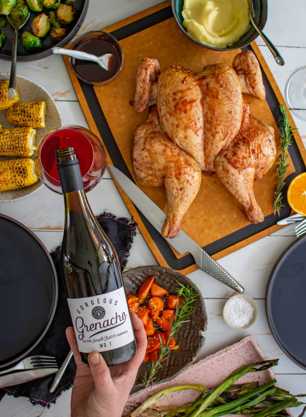 someone pouring wine with smoked spatchcock chicken below on a table