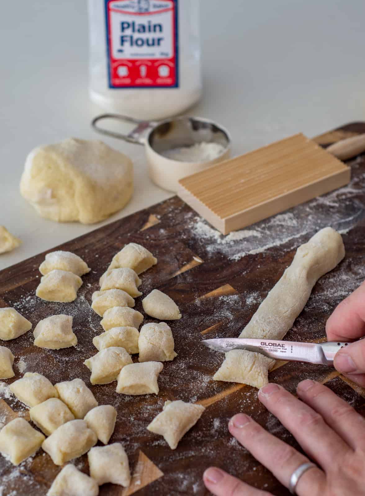 someone cutting gnocchi on a chopping board