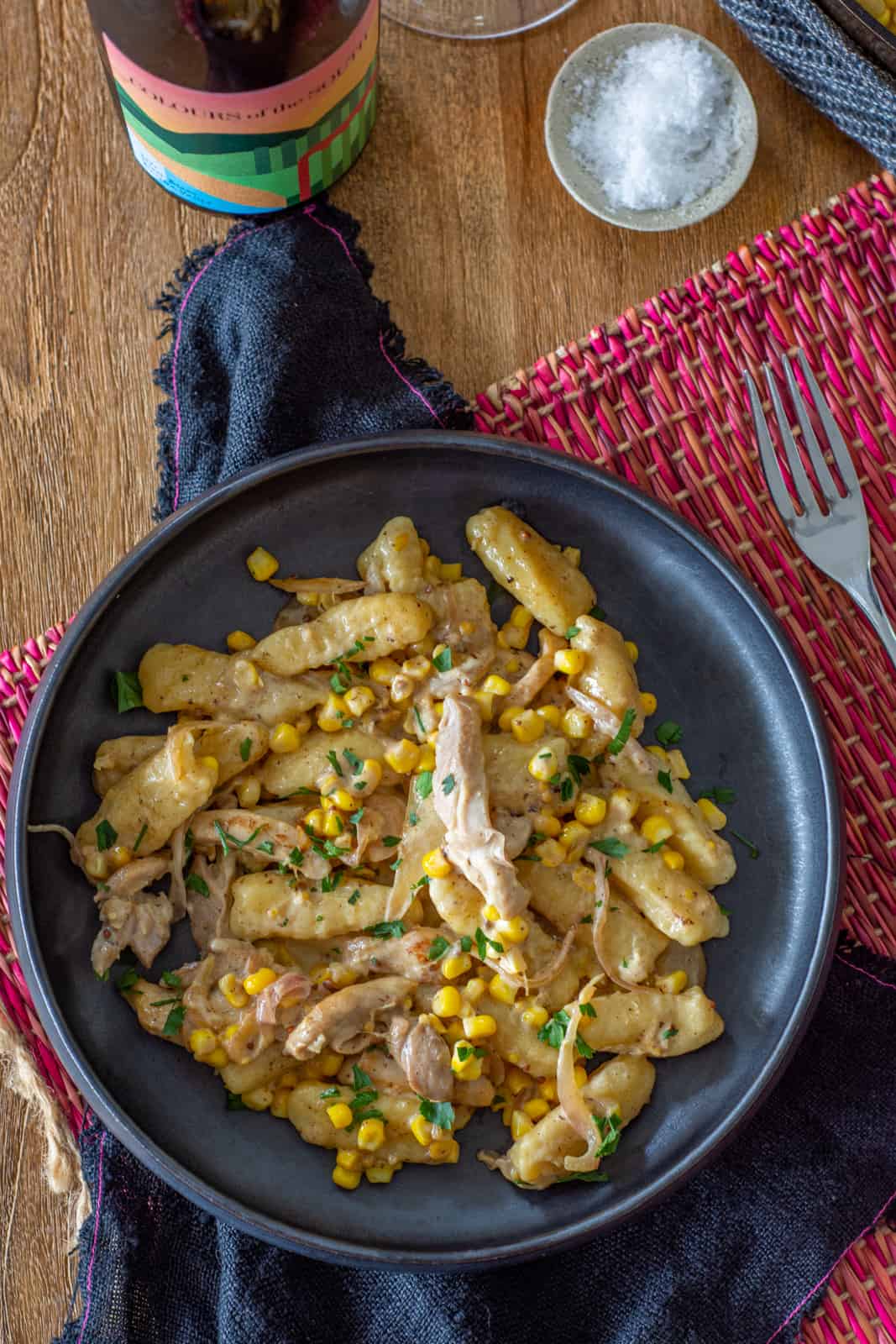 bowl of creamy gnocchi on a table with white wine bottle and salt next to it