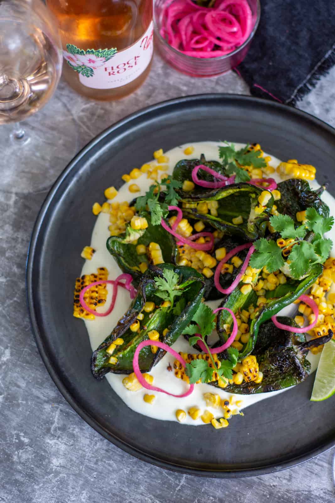 birds eye view of grilled poblano, corn and pickled onion salad with botle of flock rose beside the plate