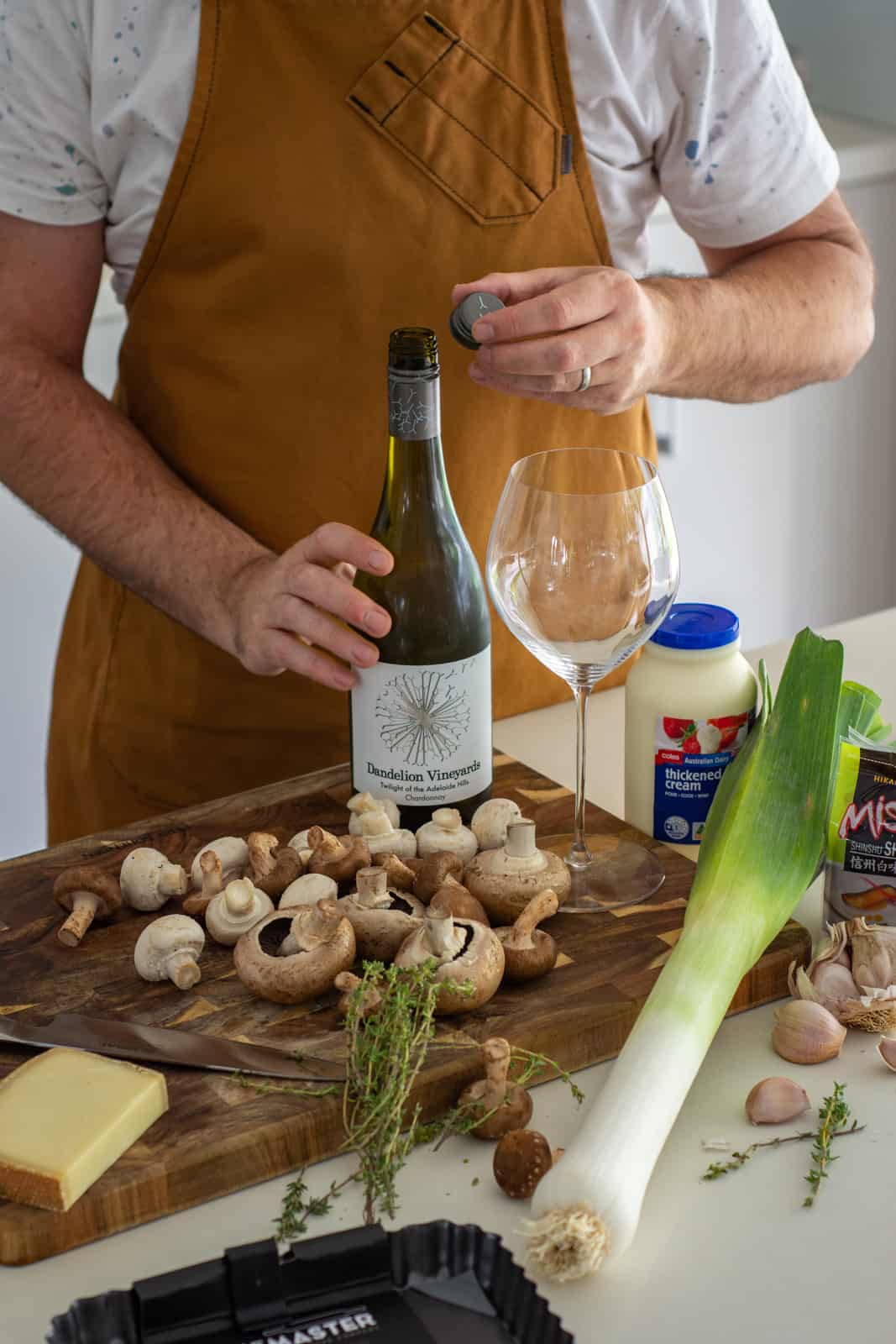Mushroom leek tartlet ingredients on a chopping board, someone opening a bottle of wine