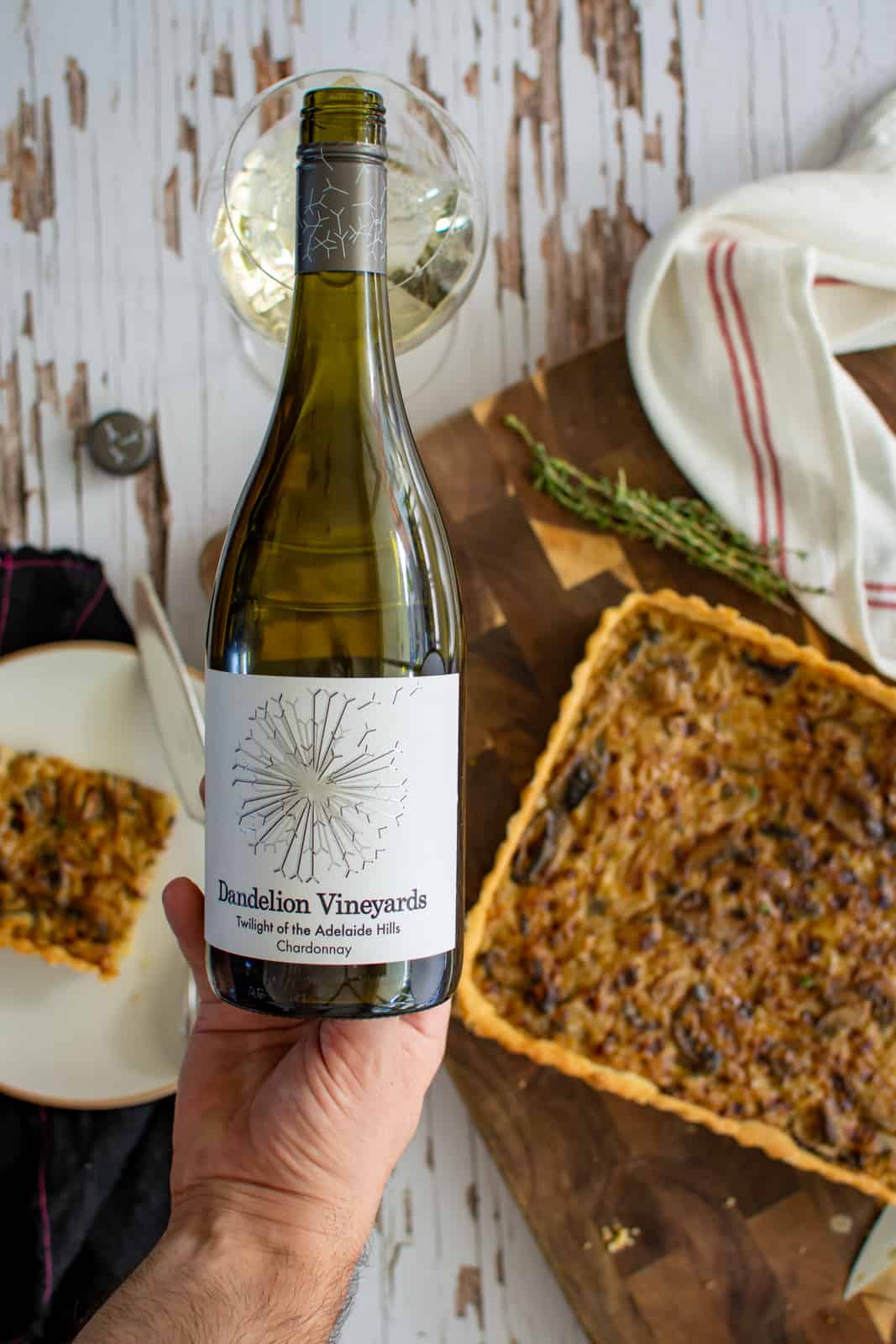 Someone pouring dandelion vineyards chardonnay with mushroom leek tartlet below