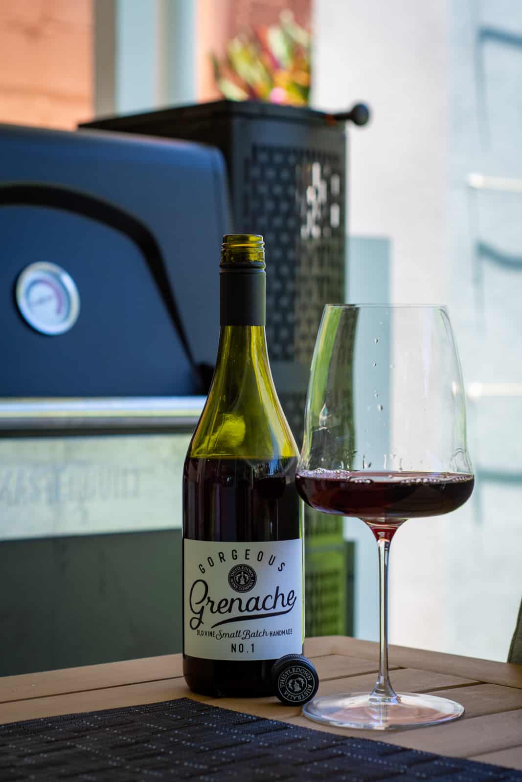 Thistledown gorgeous grenache wine on a table with BBQ behind it