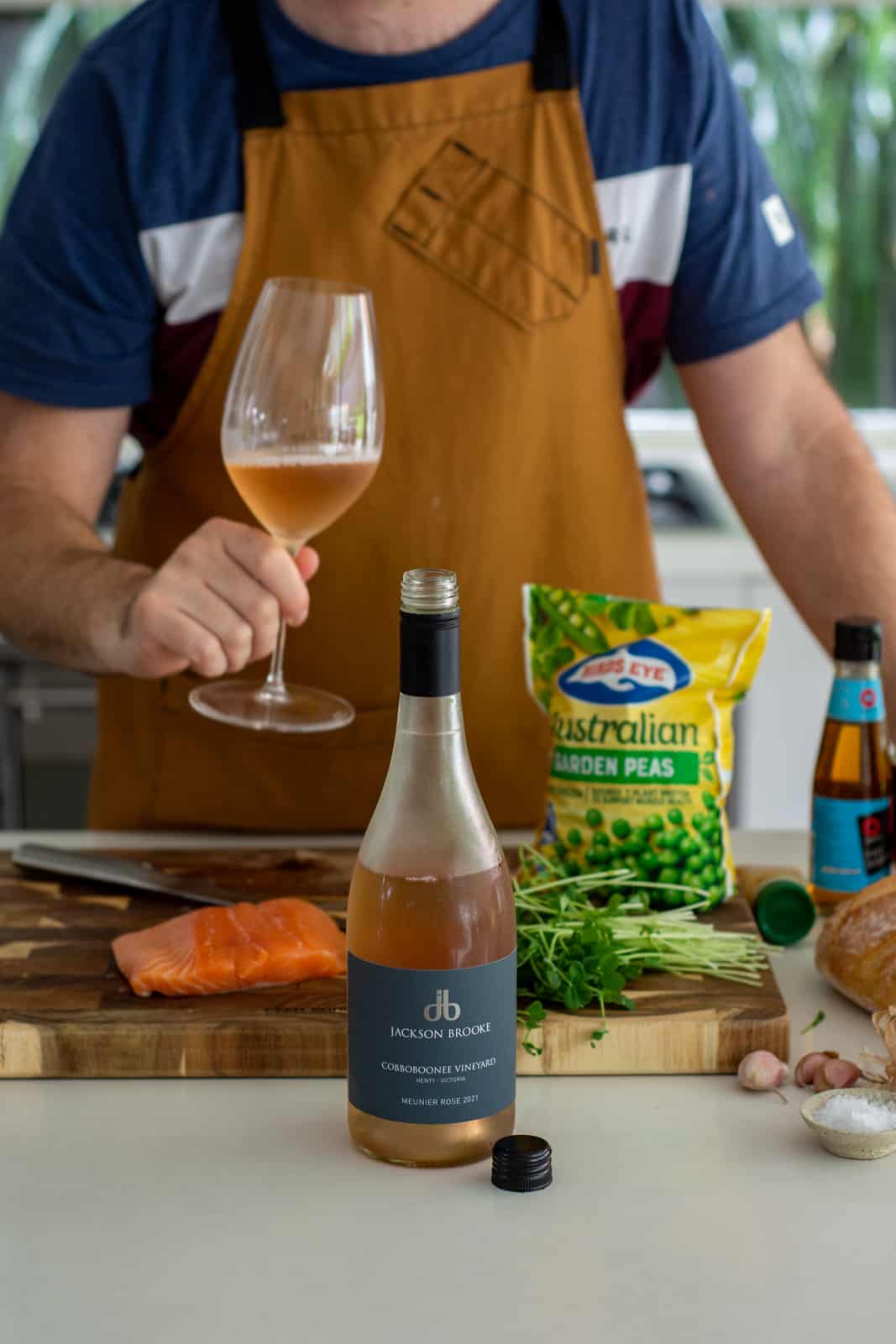 someone holding a glass of wine in the kitchen with ingredients on counter top