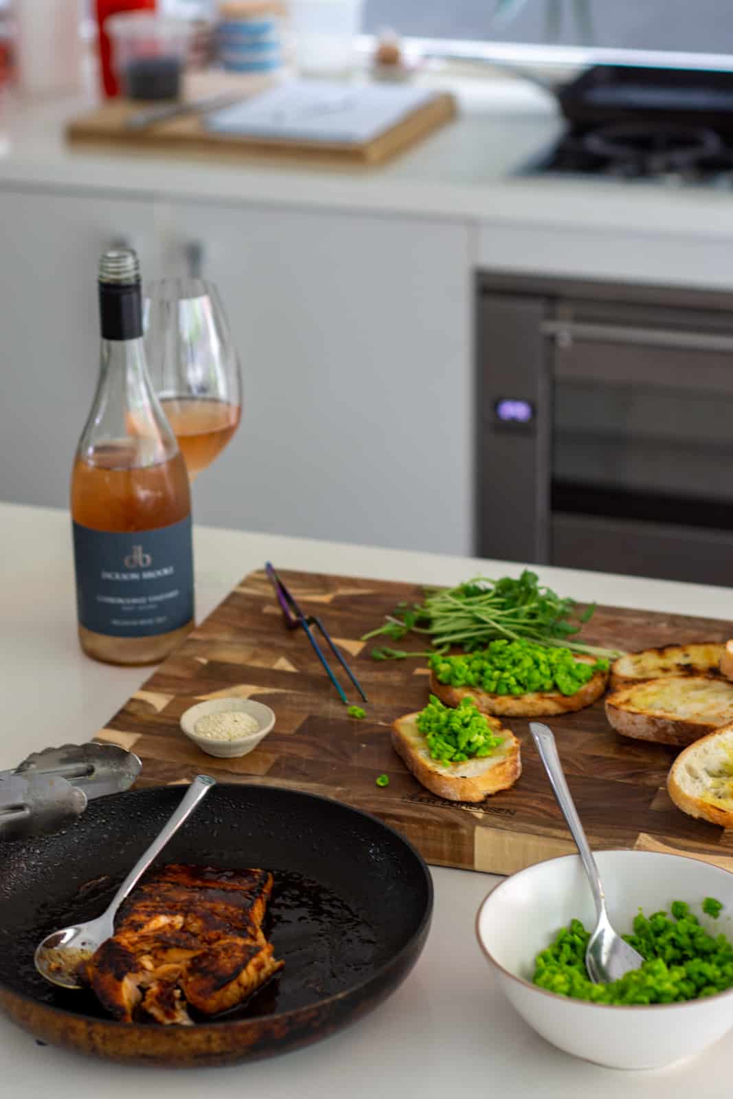 salmon in frying pan, cushed peas in a bowl and slices of toast on chopping board topped with crushed peas