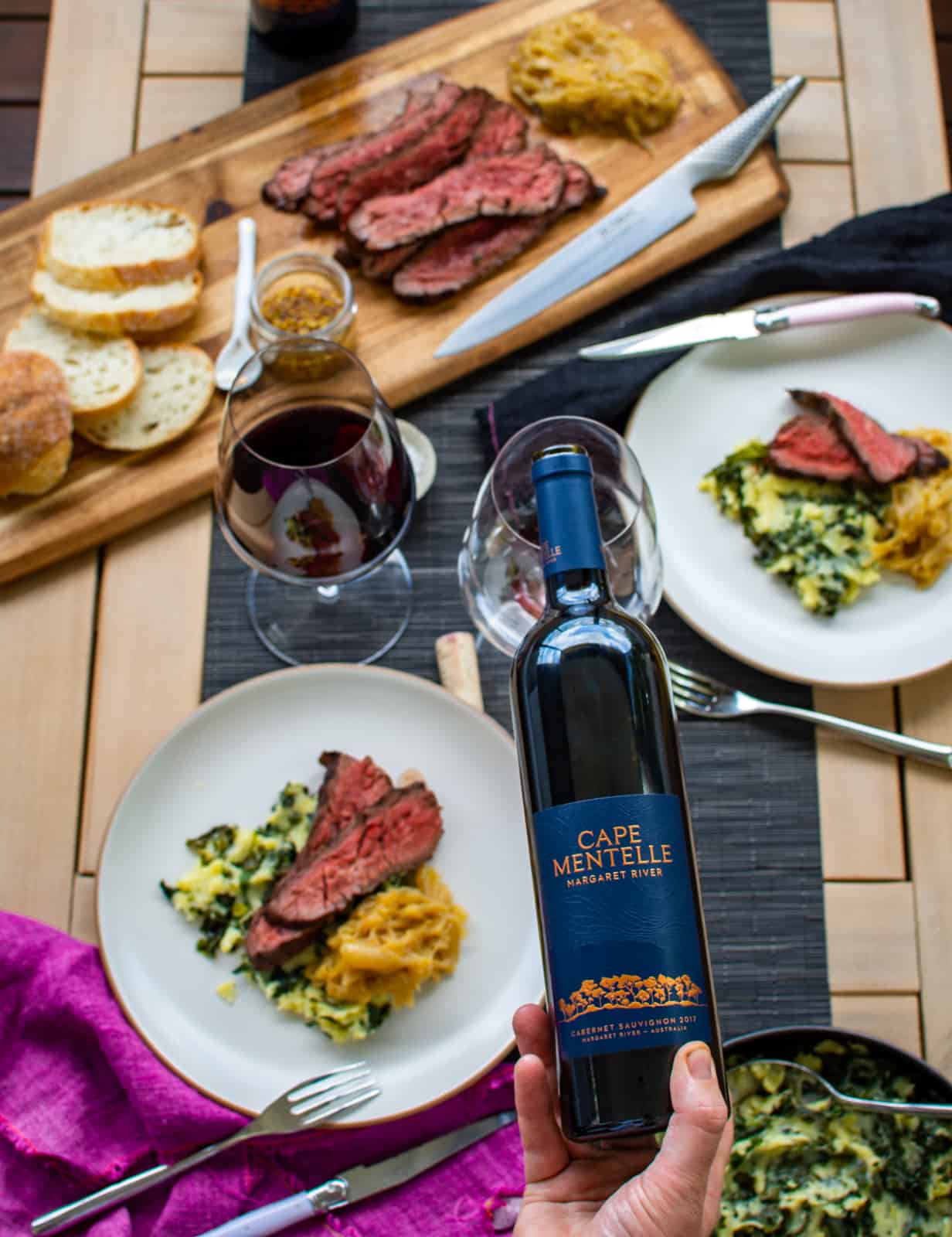 someone pouring cape mentelle wine into a glass with plates of miso steak below