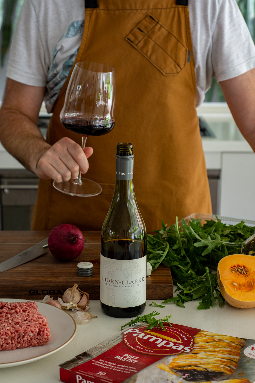 Ingredients for lamb mince tart in the kitchen with someone drinking a glass of grenache