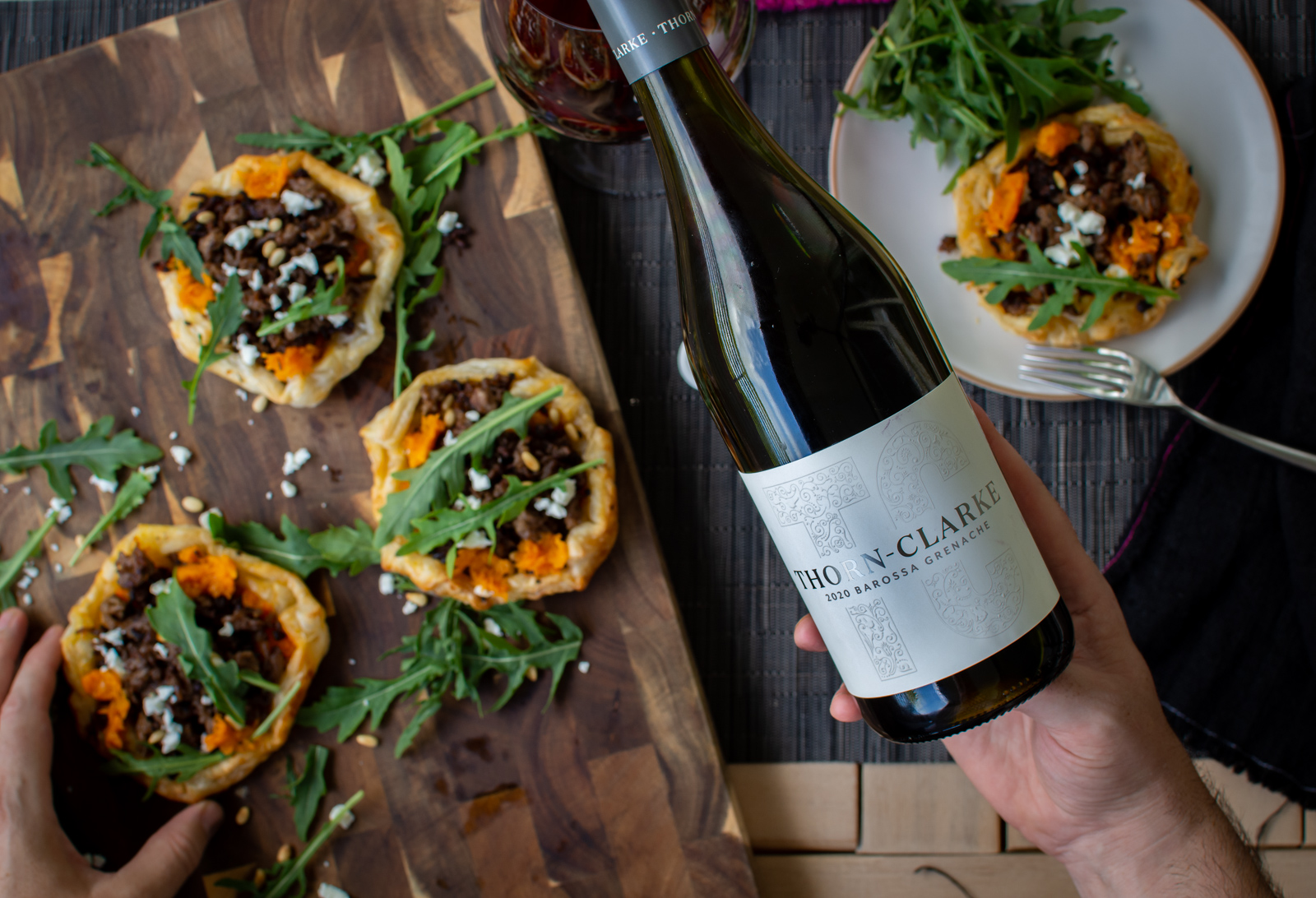 someone pouring a glass of grenache and someone picking a lamb tart of a plate below