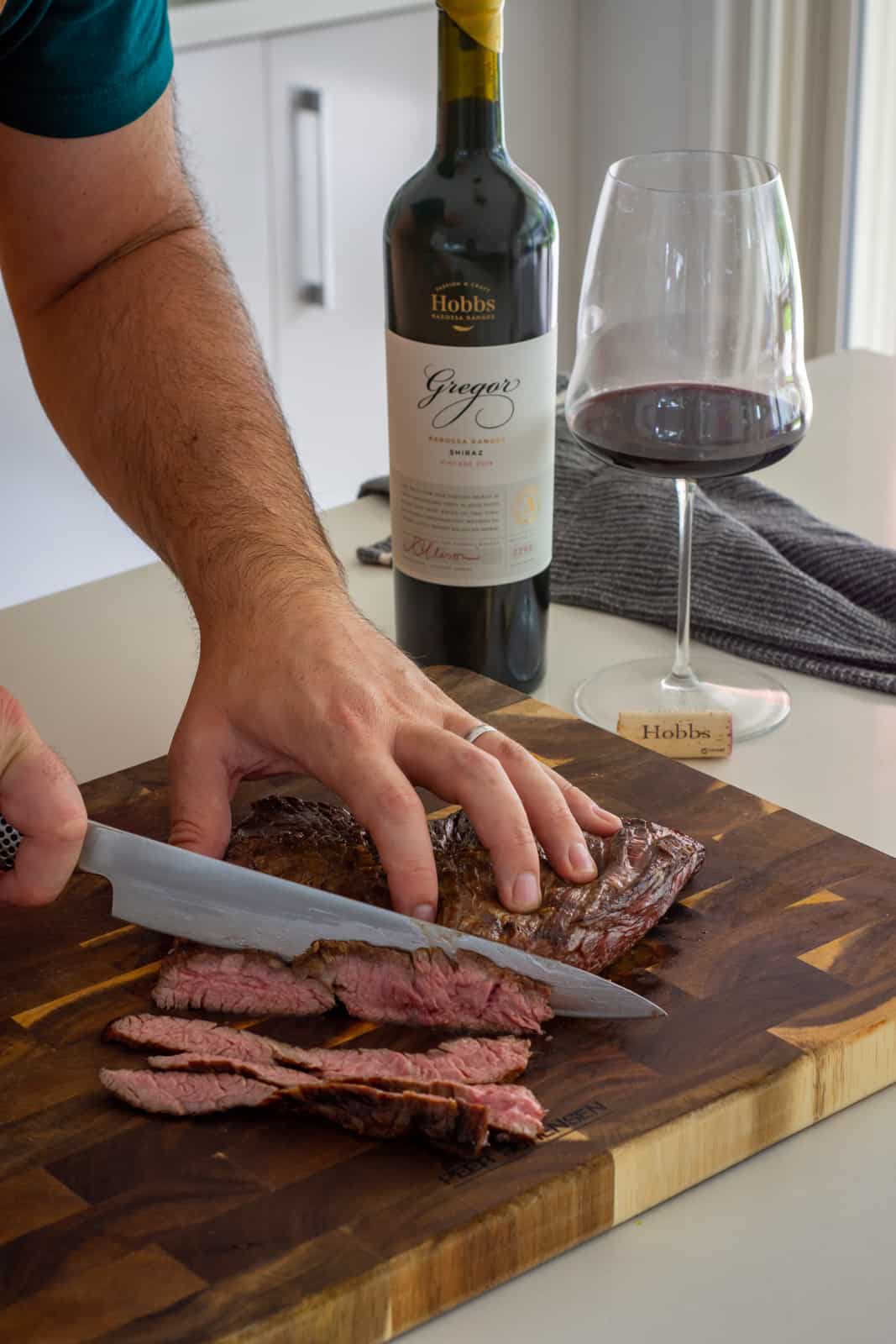 someone slicing flap steak with wine beside them 