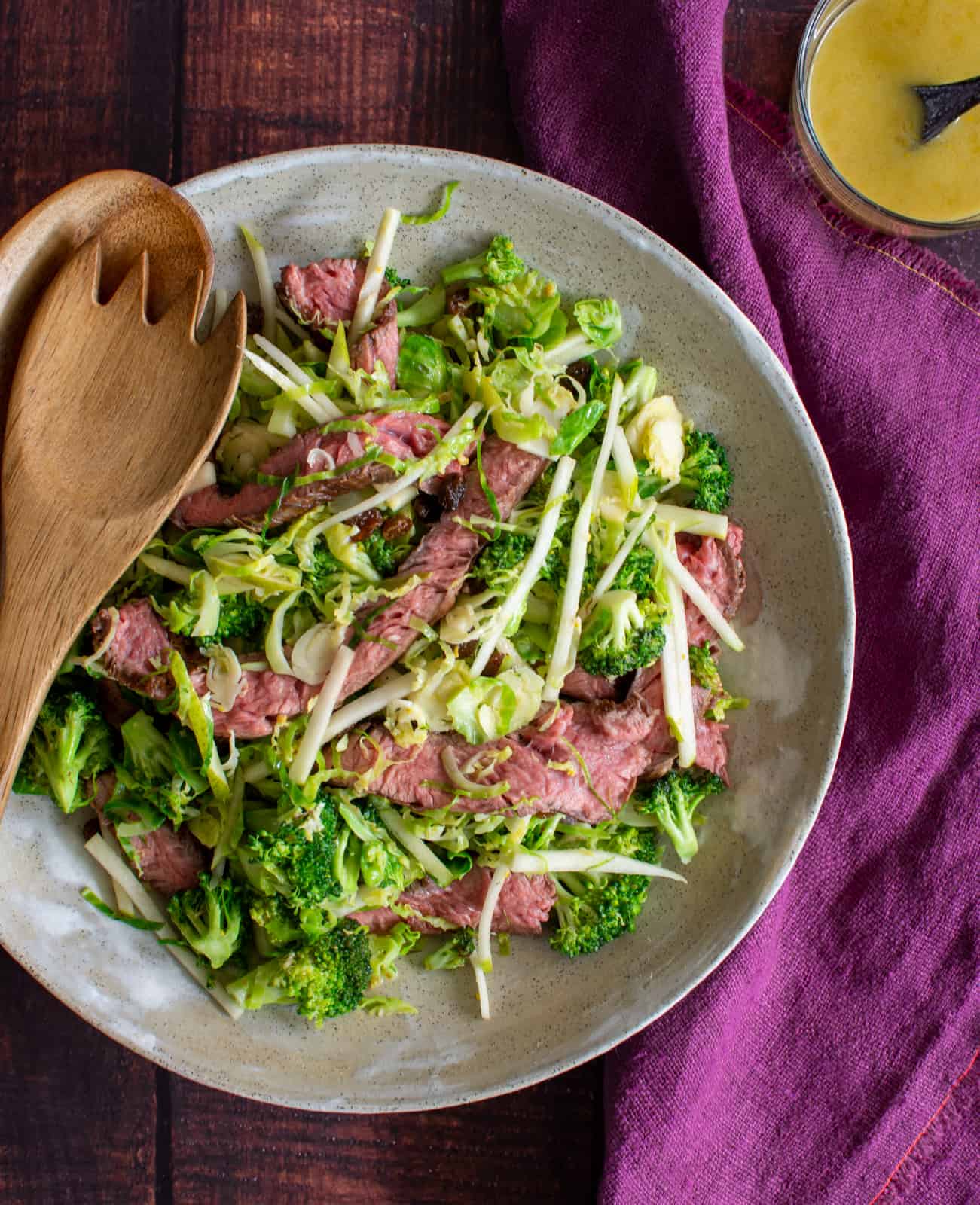 Birdseye view of broccoli, steak & pear salad with dressing next to it 