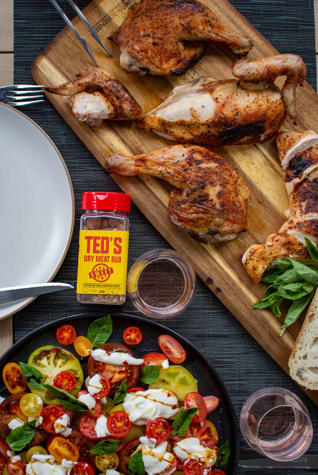 Birdseye view of BBQ chicken on a board with a tomato burrata salad next to it