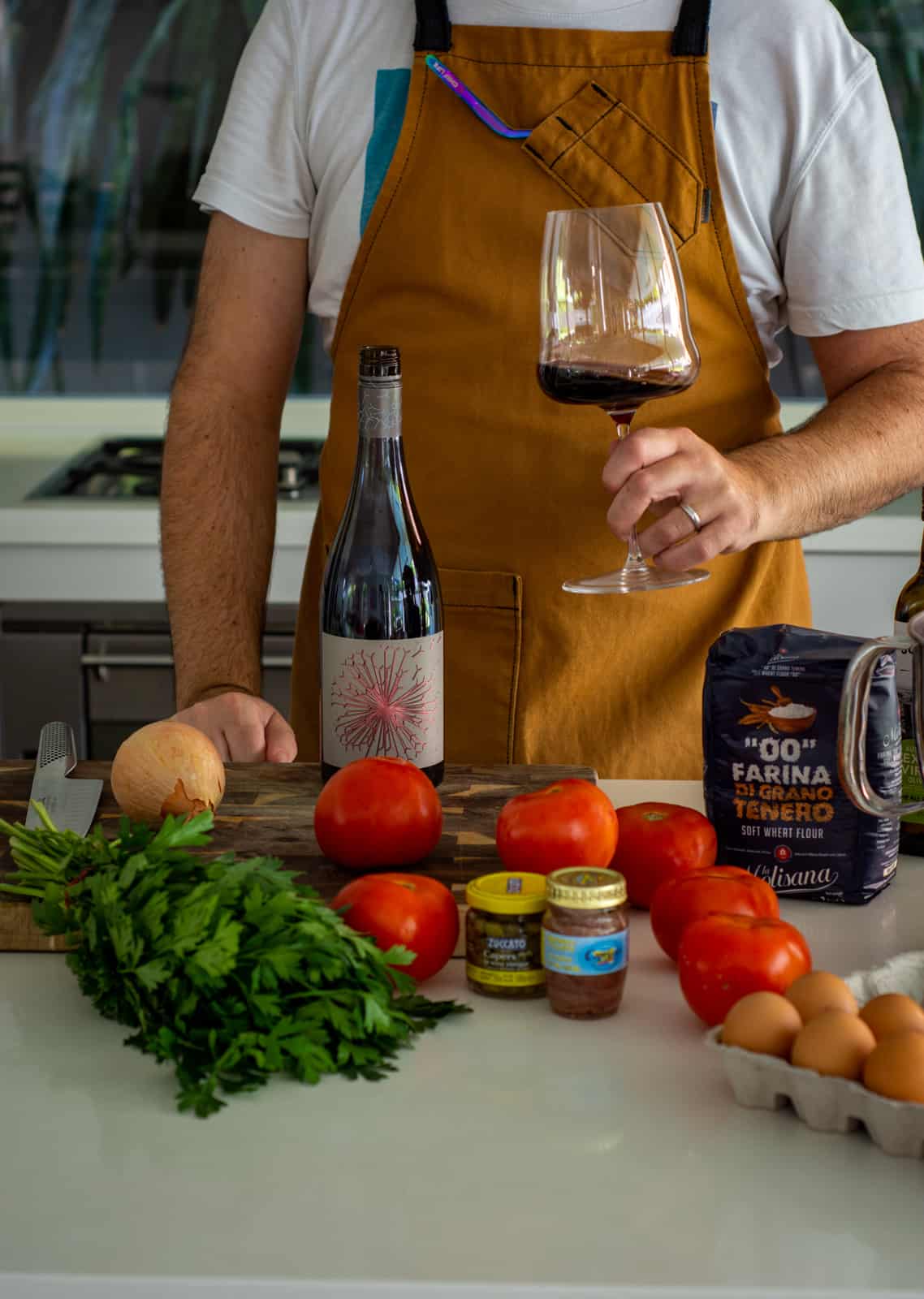 Spagahetti w/ smoked tomato sauce ingredients on kitchen counter with someone drinking a glass of red wine