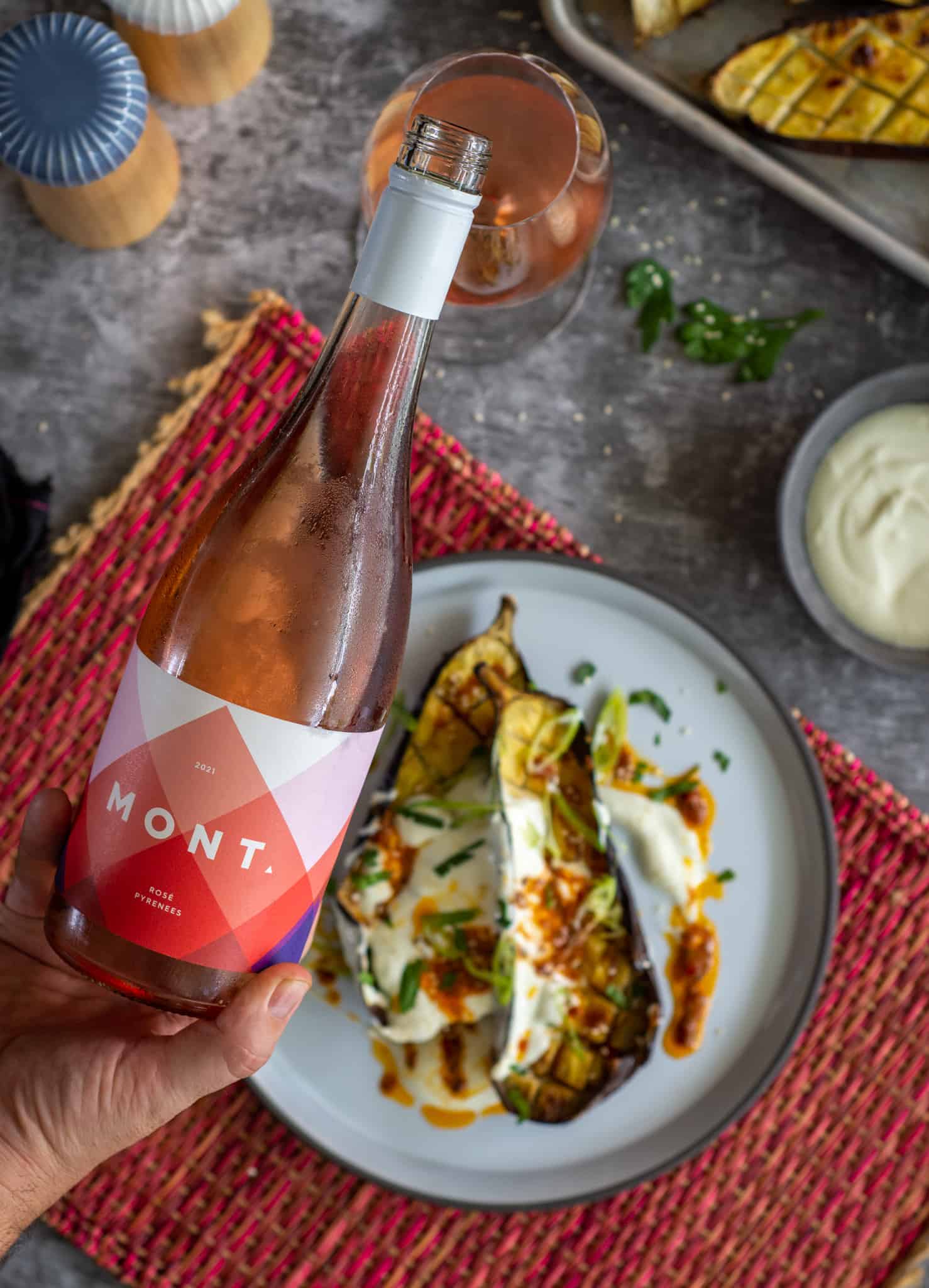 Someone pouing a glass of rose wine with roasted aubergine and harissa butter on plate below