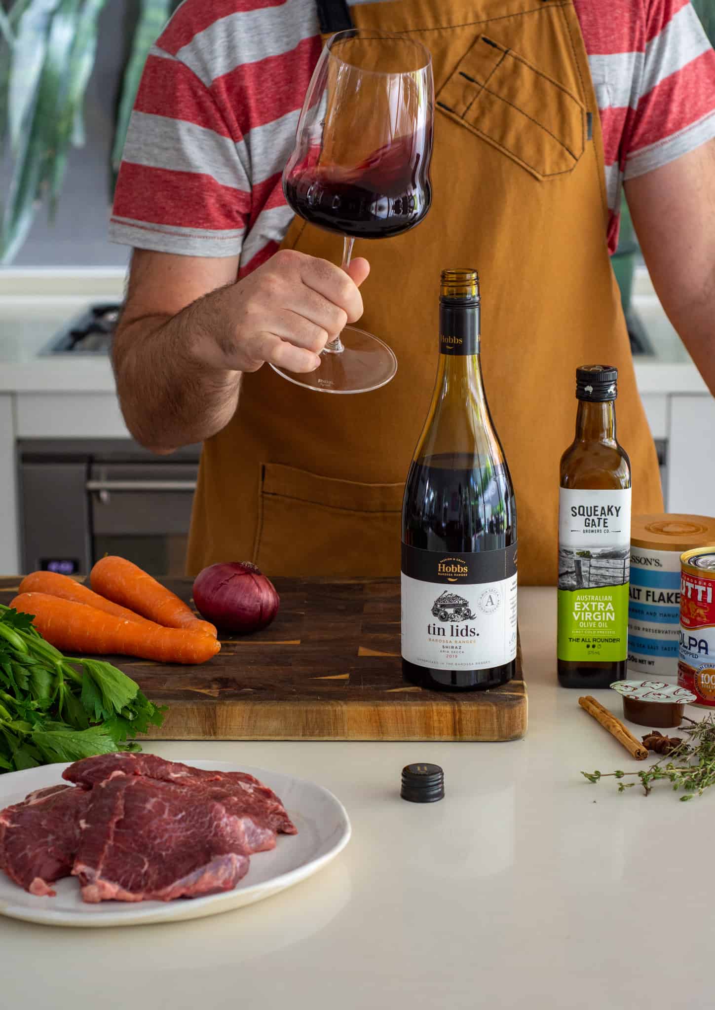 Someone swirling a glass of wine in the kitchen with ingredients around them