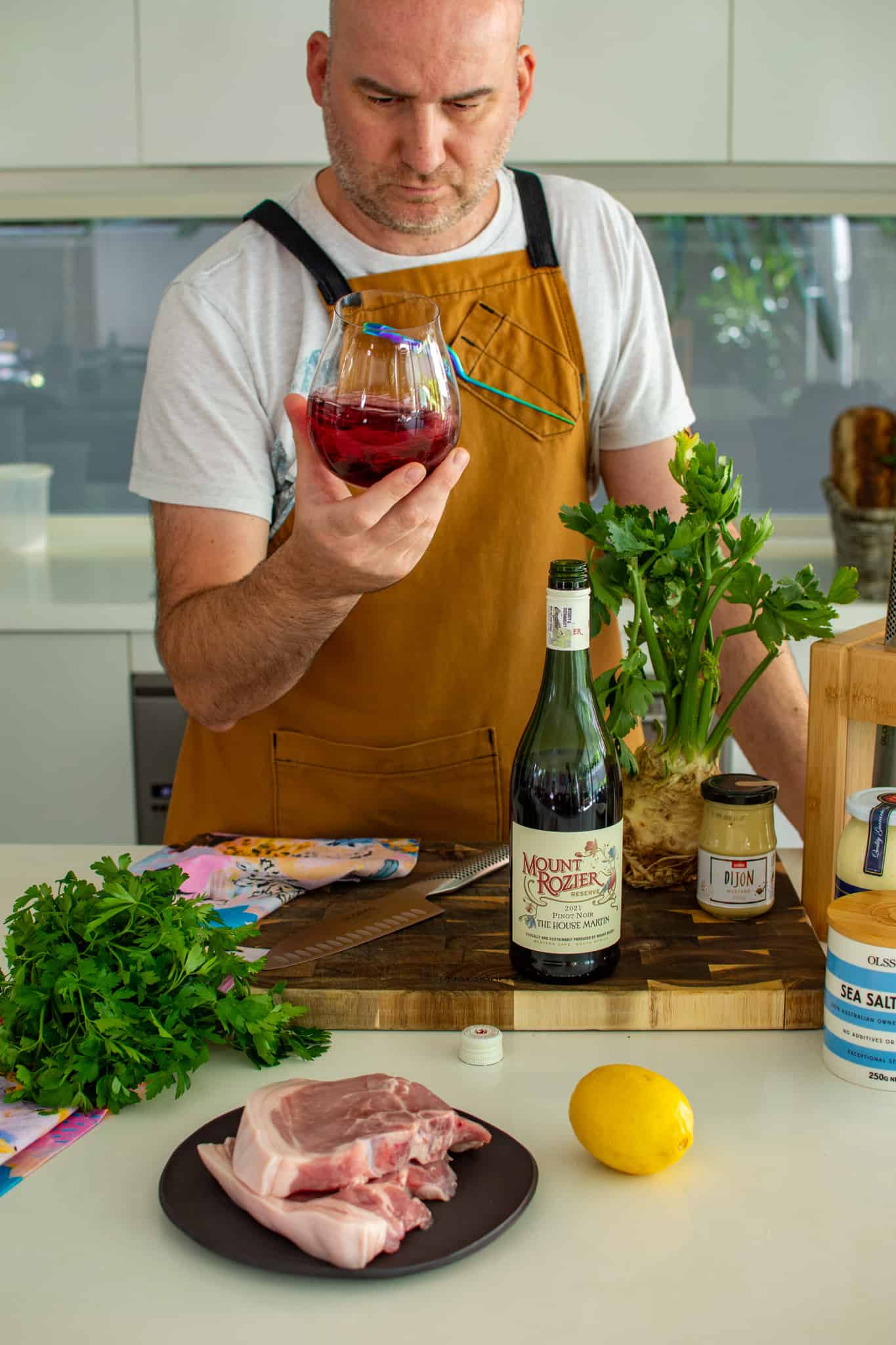 Someone swirling wine in the kitchen with food on chopping board