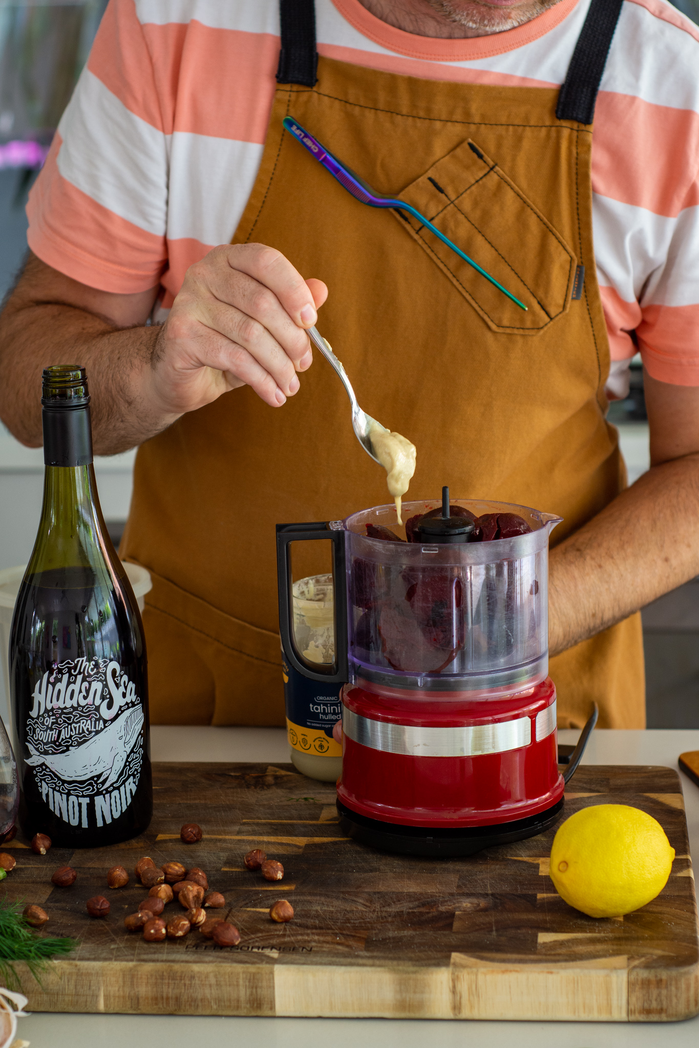 someone making beetroot hummus in the kitchen with wine beside them on the counter top