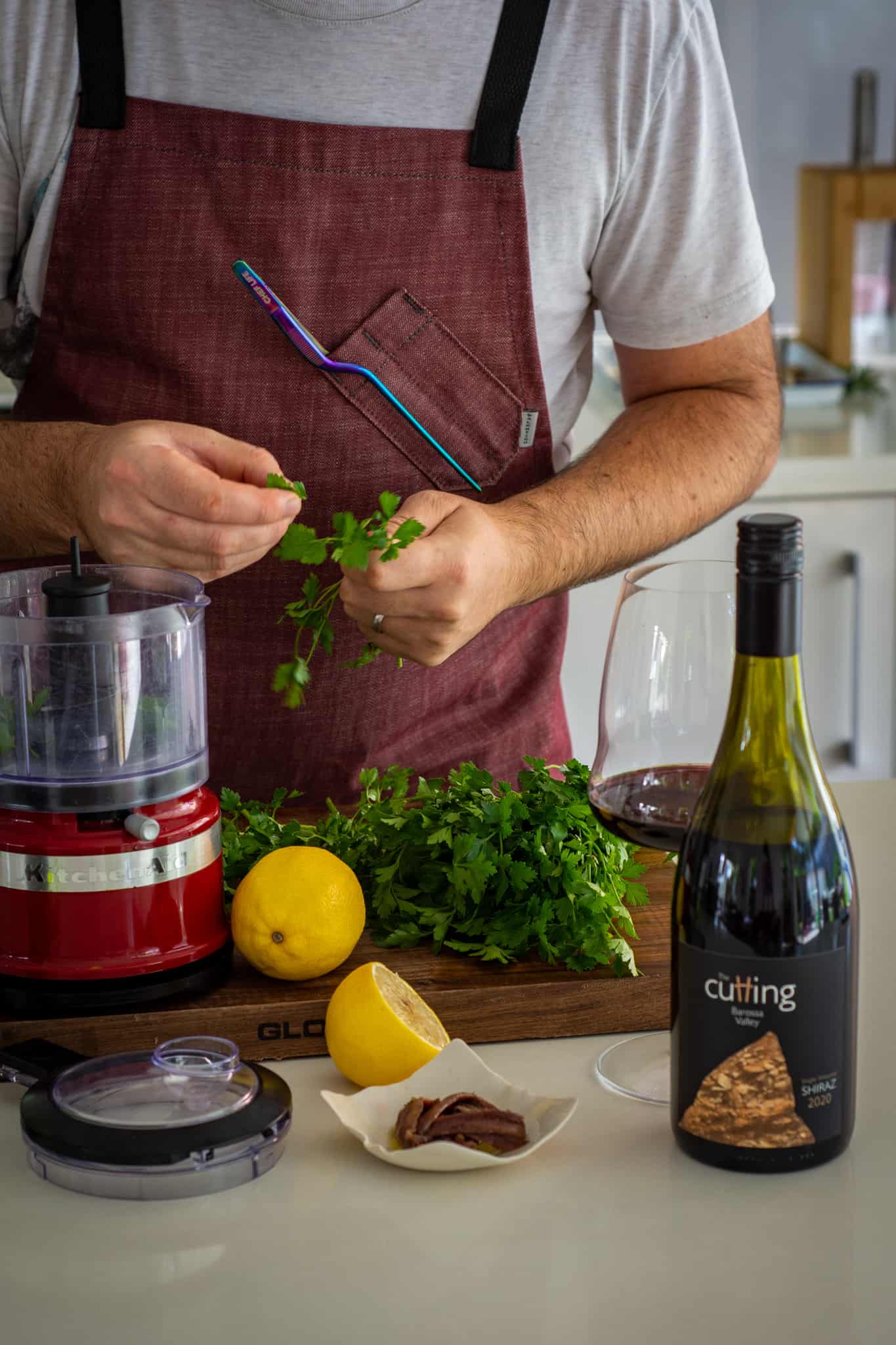 Someone picking parsley in the kitchen with a blender, ingredients and a bottle of wine on counter top