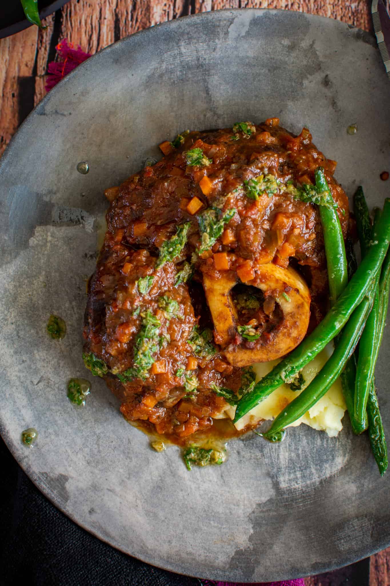 Brasied beef ossobucco with mashed potatoes and green beans on a plate