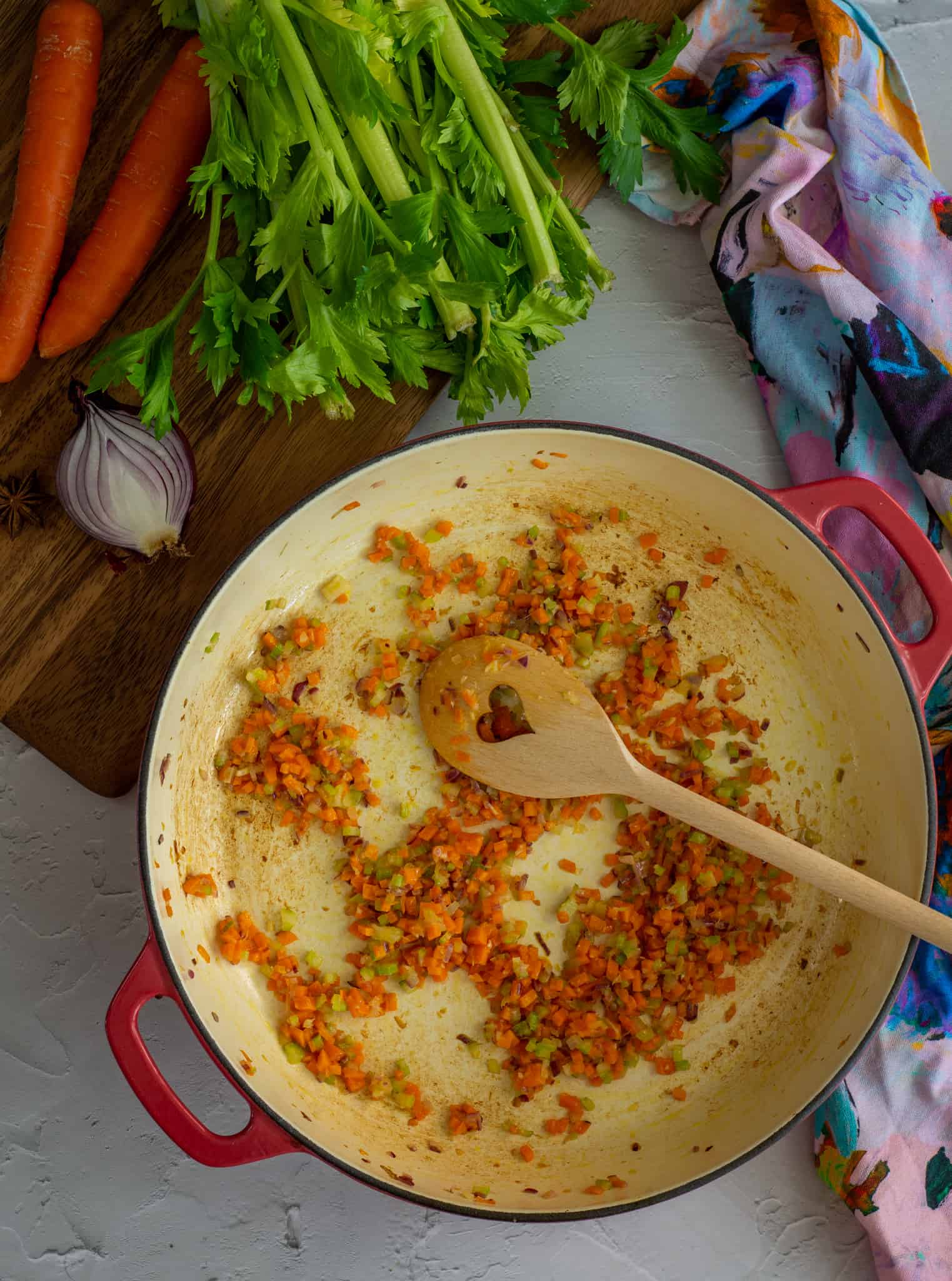 A heart shaped spoon being used to stir vegetables being cooked in pan