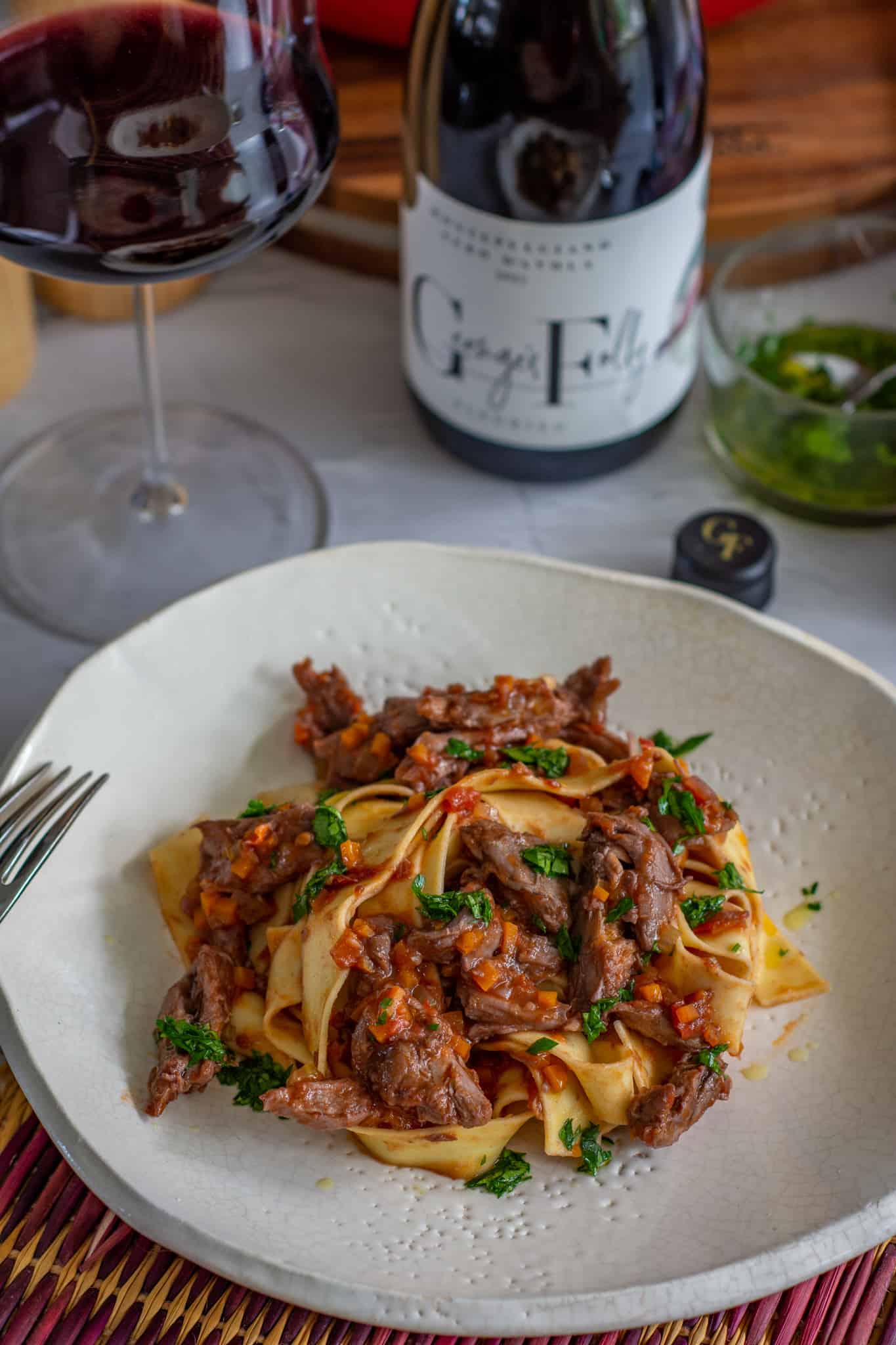 Duck ragu on a plate with wine glass and wine behind it on a table 