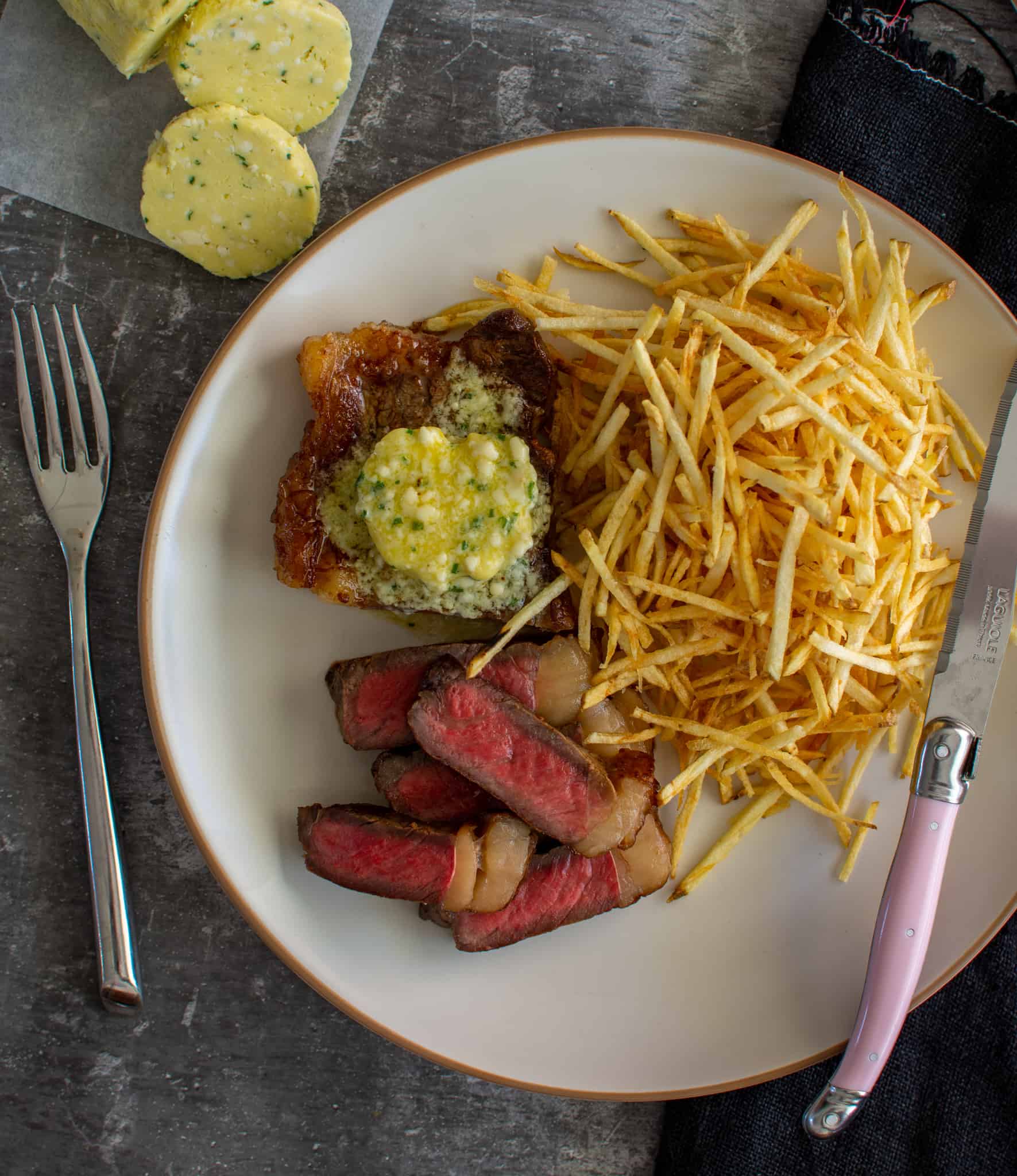 medium rare sriploin steak, shoestring fries and garlic butter on a plate