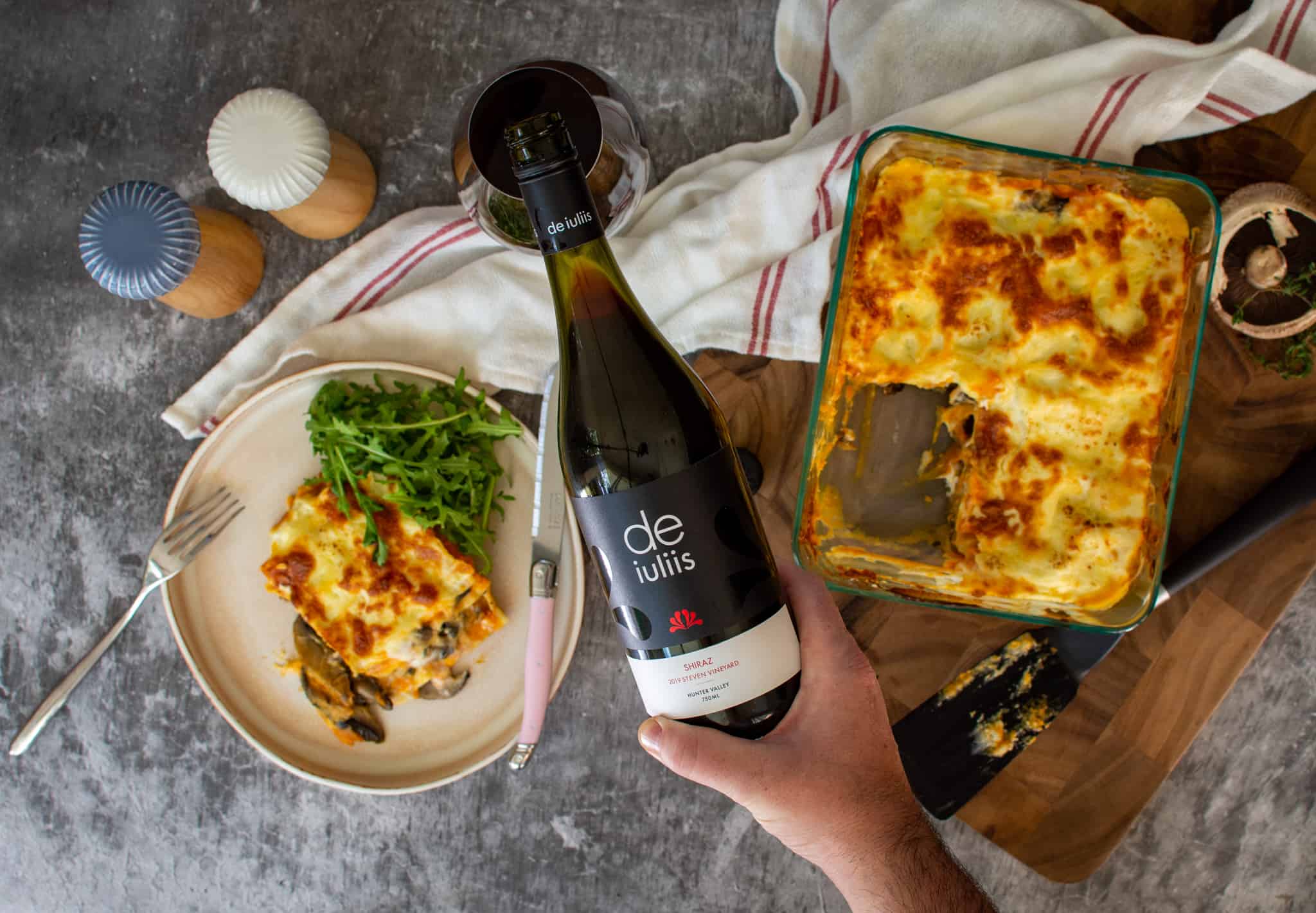 Birdseye view of someone pouring wine w/ lasagne on plates below