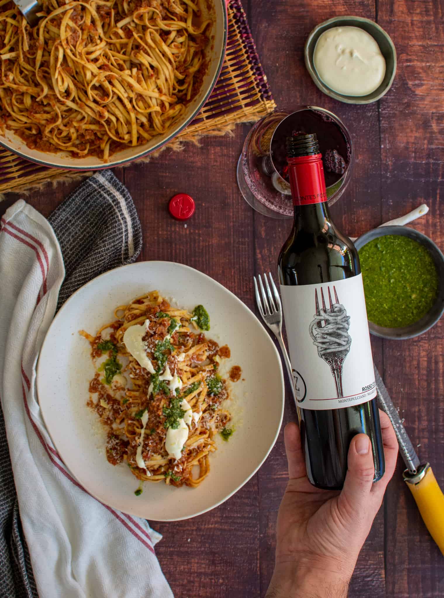 someone pouring wine into a glass with a bowl of pasta next to it.
