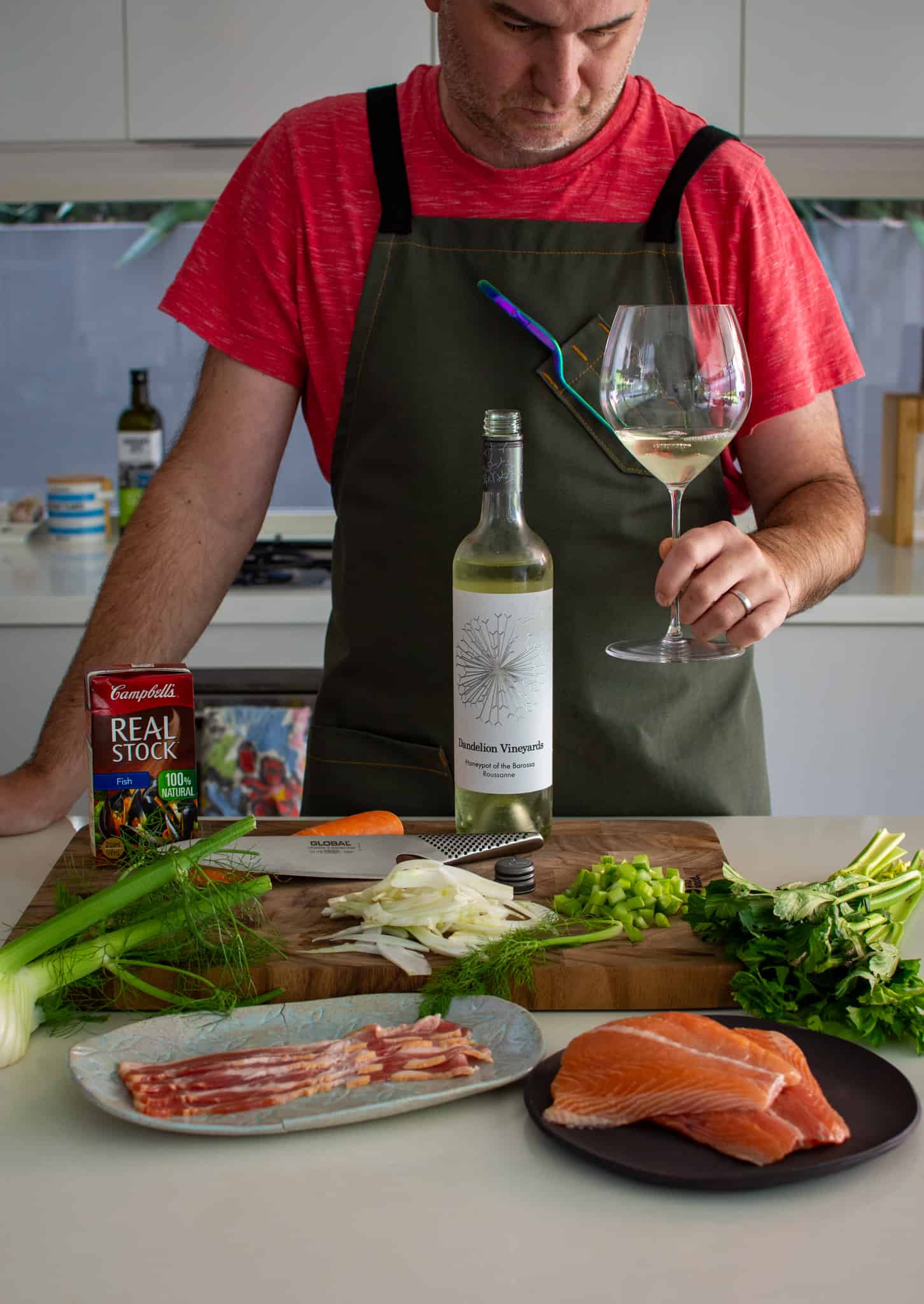 someone looking at a glass of wine in the kitchen with ingredients on counter top