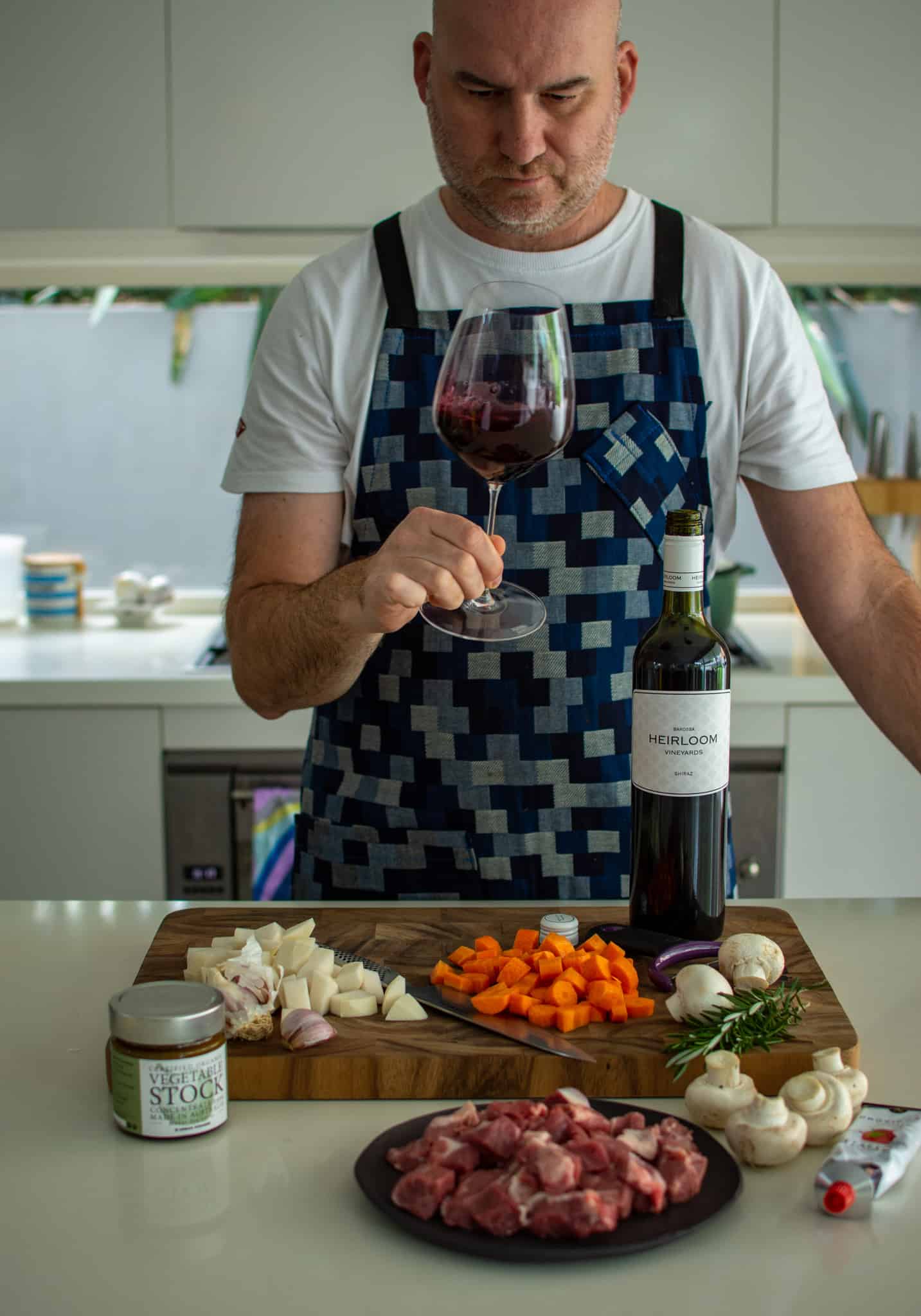 someone in the kitchen holding a glass of wine with food on the counter top