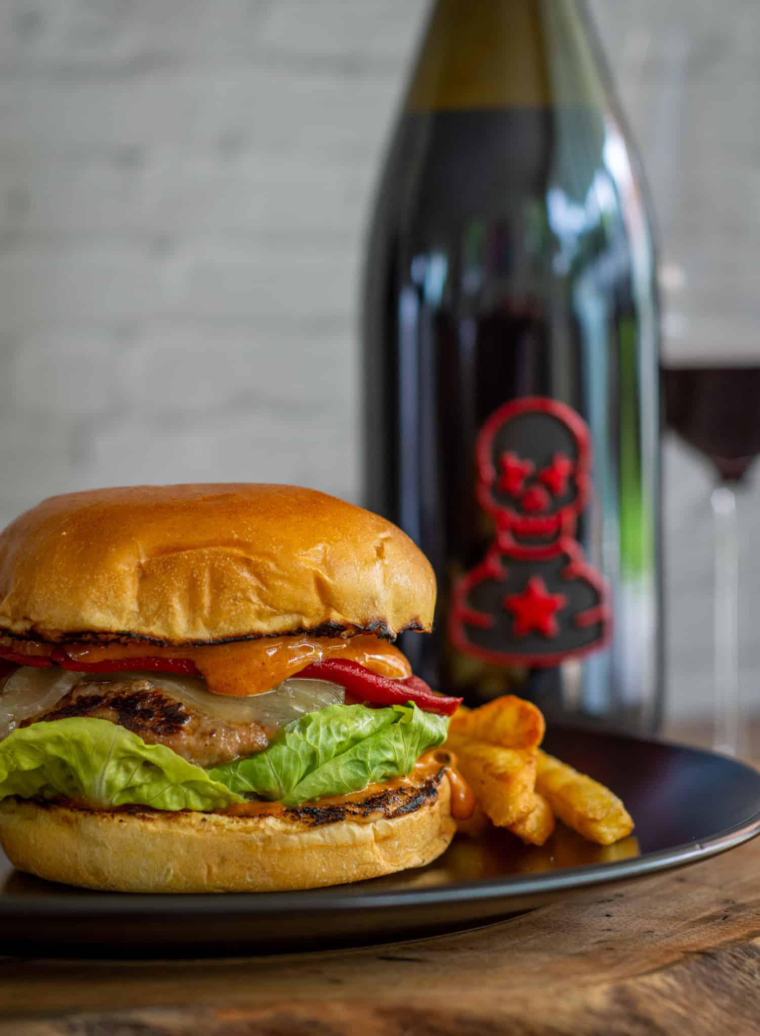 Close up of spanish burger with manchego, piquillo peppers and smoked paprika aioli. Bottle of wine next to the burger