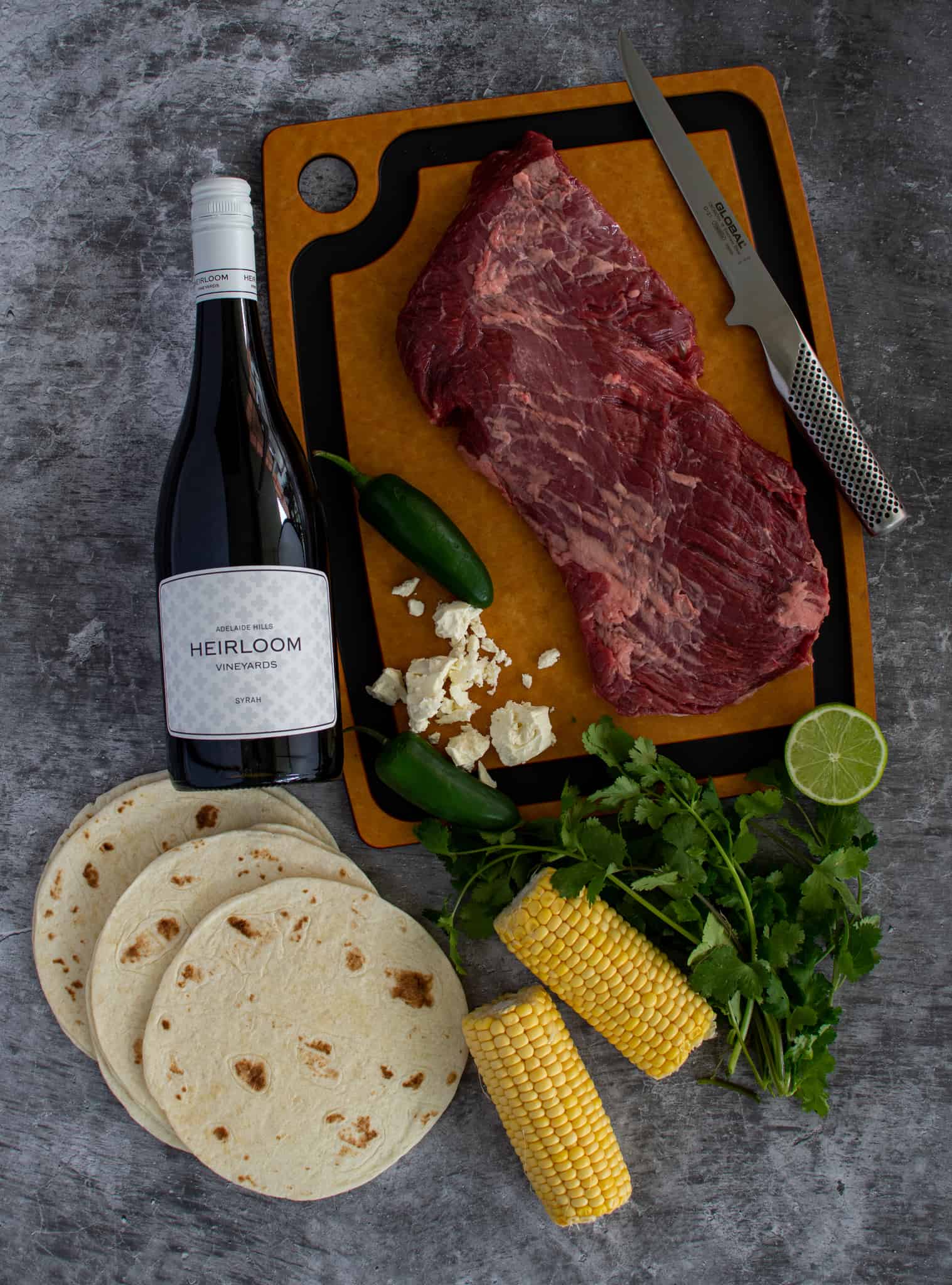 birdseye view of ingredients for grilled steak tacos with a bottle of wine next to the ingredients