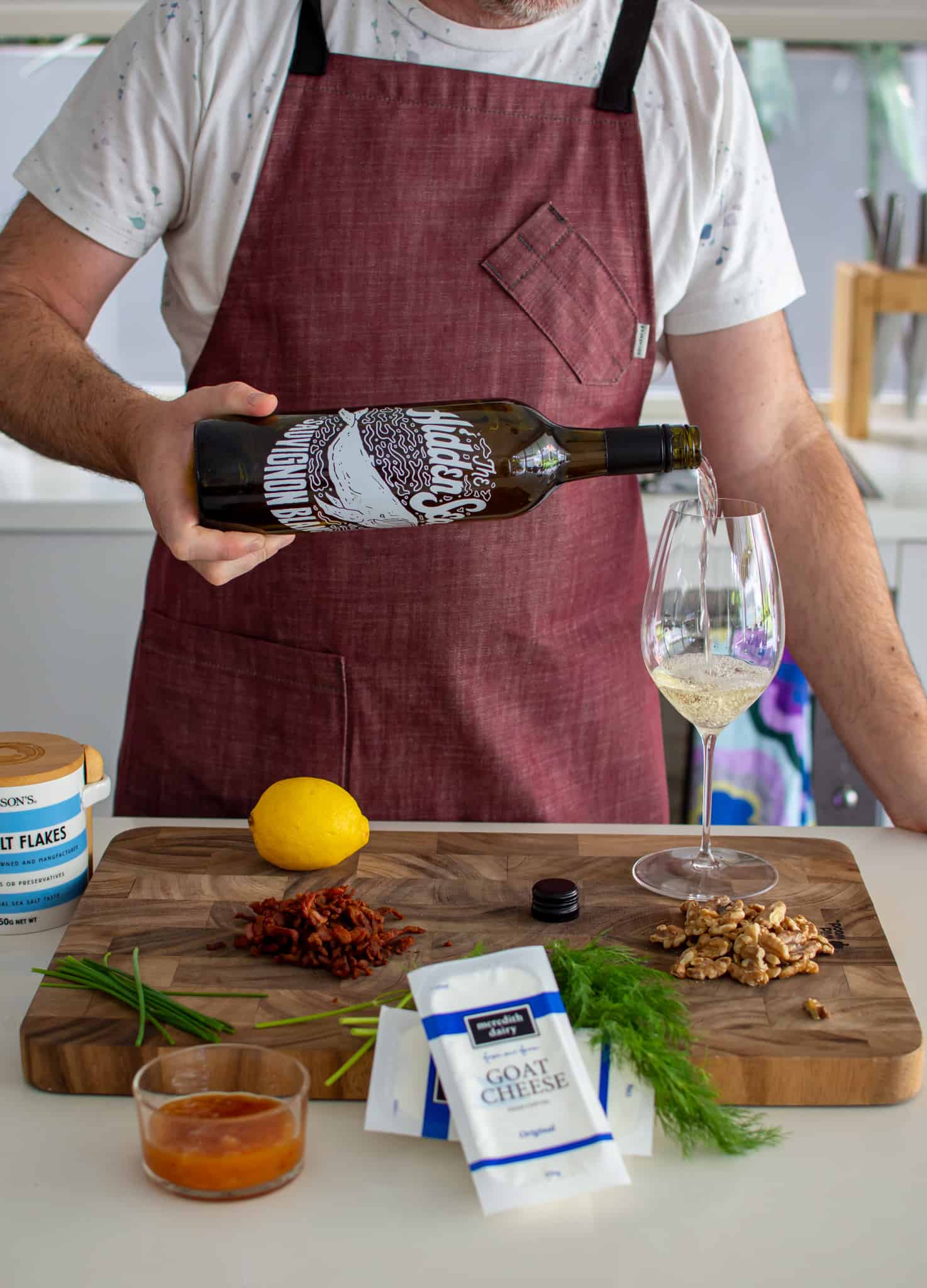 someone pouring a glass of wine in the kitchen with food on counter top