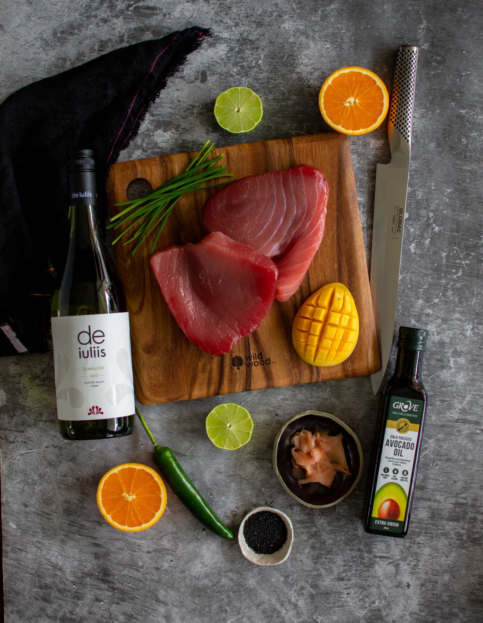tuna crudo ingredients on chopping board with bottle of wine and global sashimi knife beside them