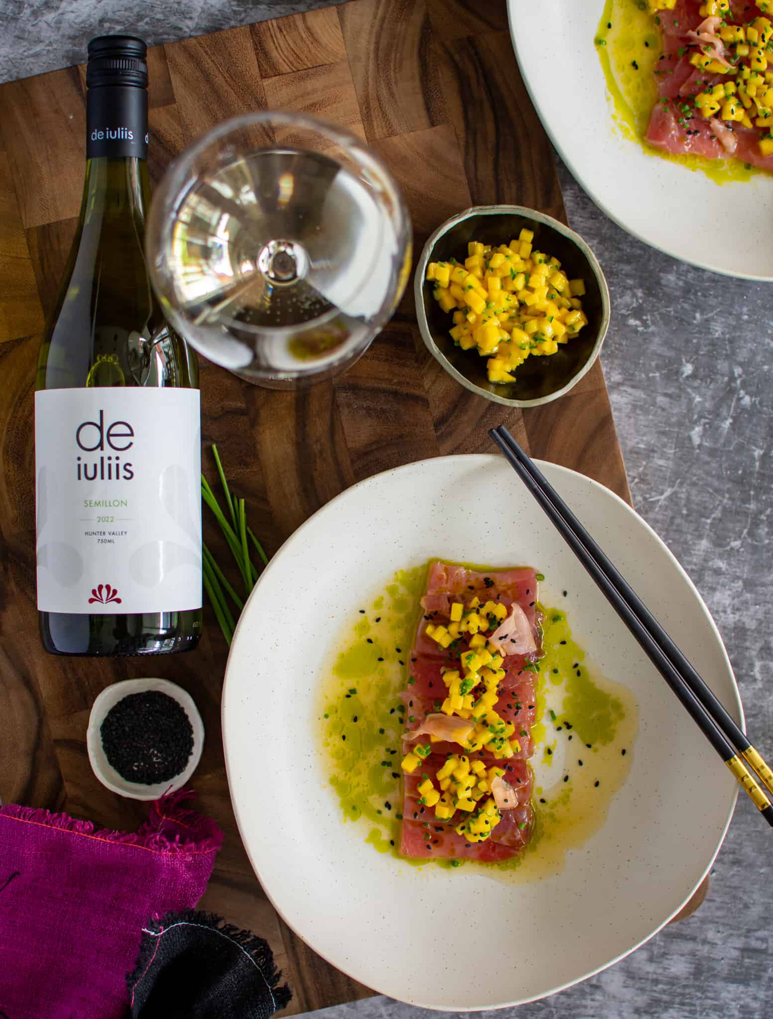 tuna with mango chilli salsa on a plate with a bottle of wine lying next to it. The plate has black chopsticks and napkins lying next to it