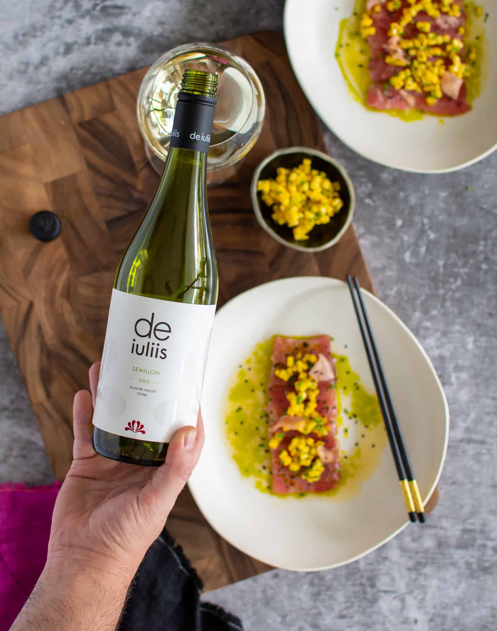 birds eye view of someone pouring De iuliis semillon into a glass with a plate of tuna crudo below