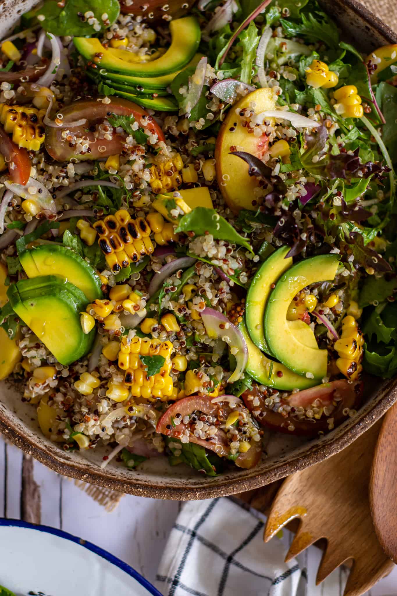 birdseye view of grain salad in a bowl with napkin and wooden salad tongs beside