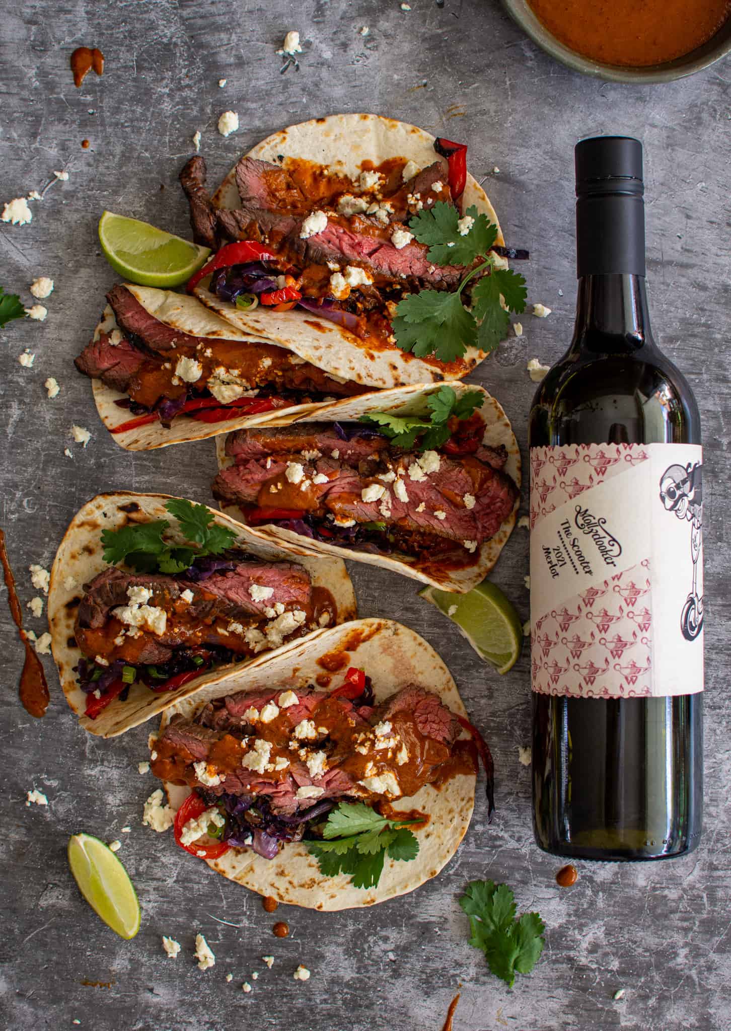 Birdseye view of multiple tacos on a counter top with a bottle of wine beside them