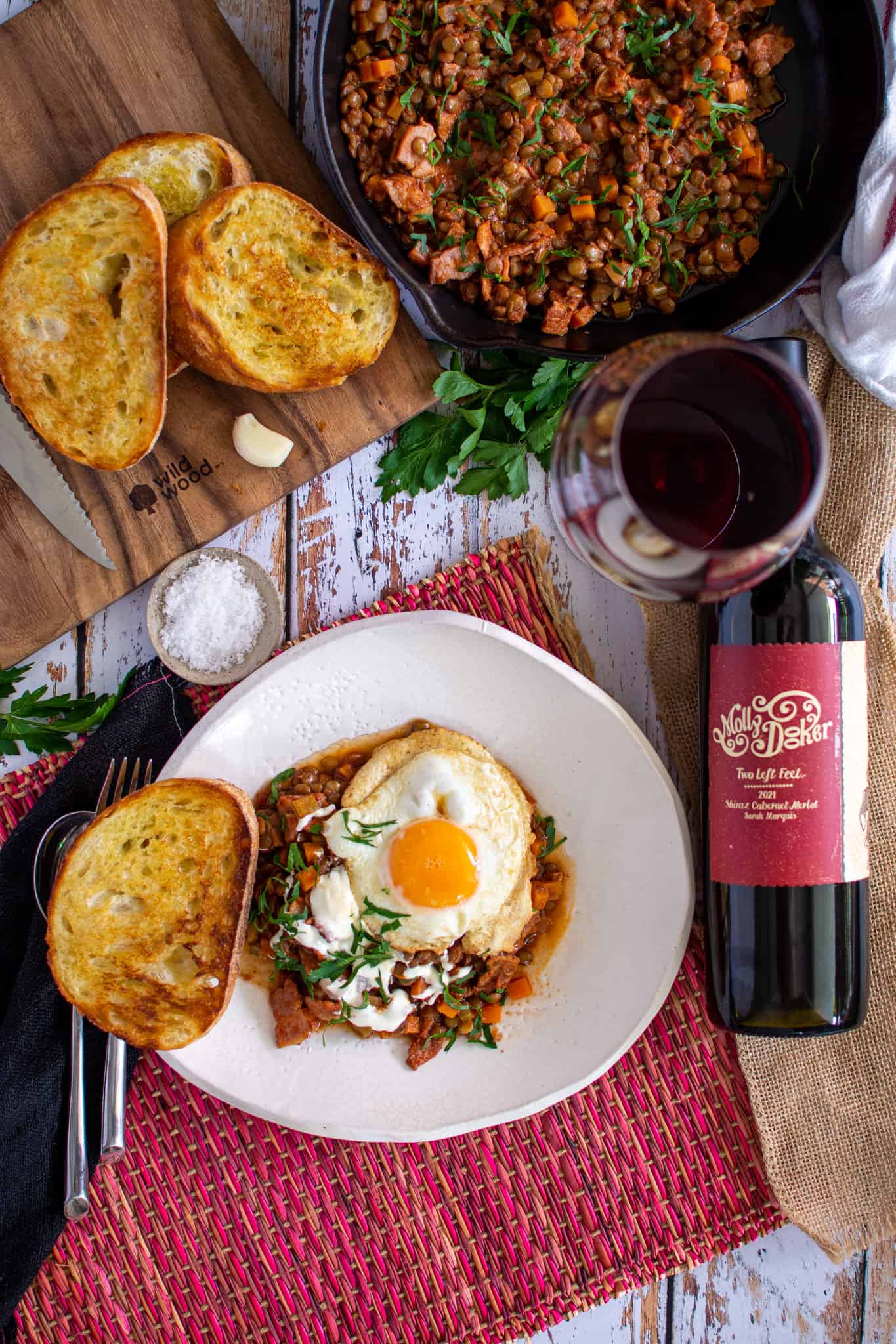 birdseye view of bacon lentil stew with a bottle of wine next to it and some crusty bread too