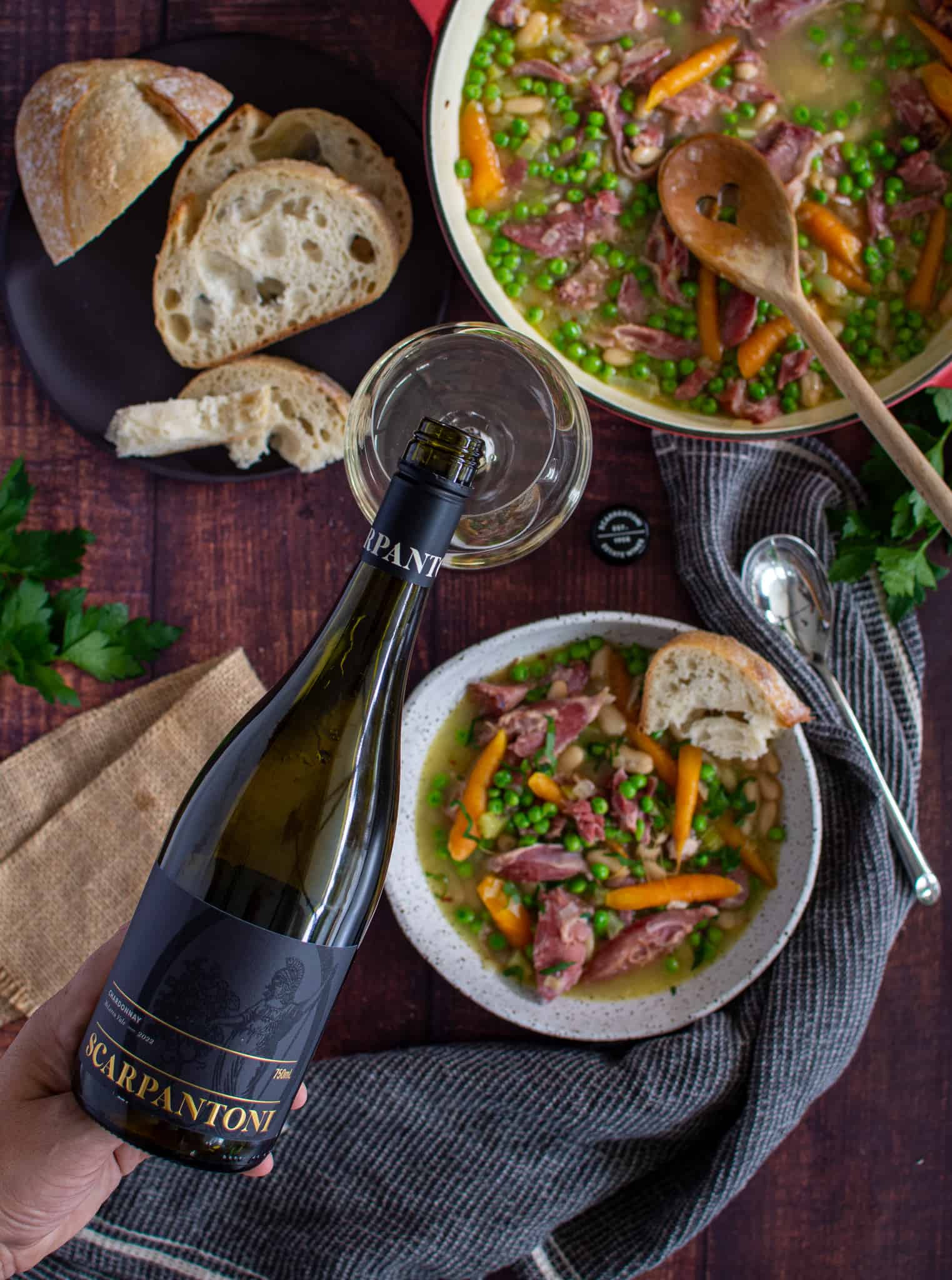 birdseye view of someone pouring wine into a glass witha bowl of stew below
