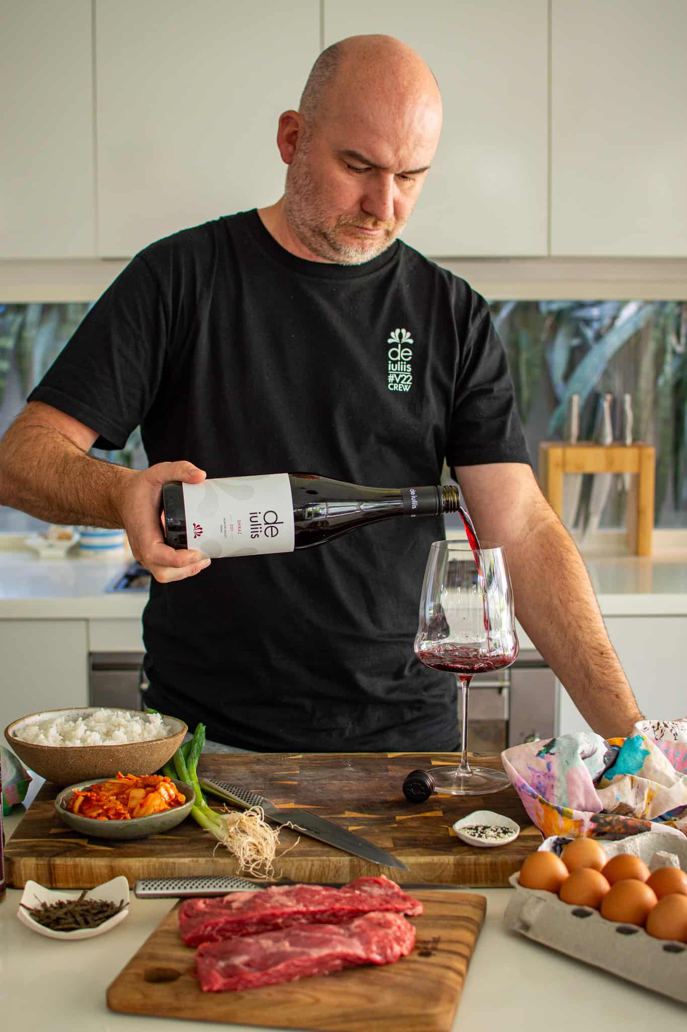 someone pouring a glass of wine in the kitchen with food on counter top